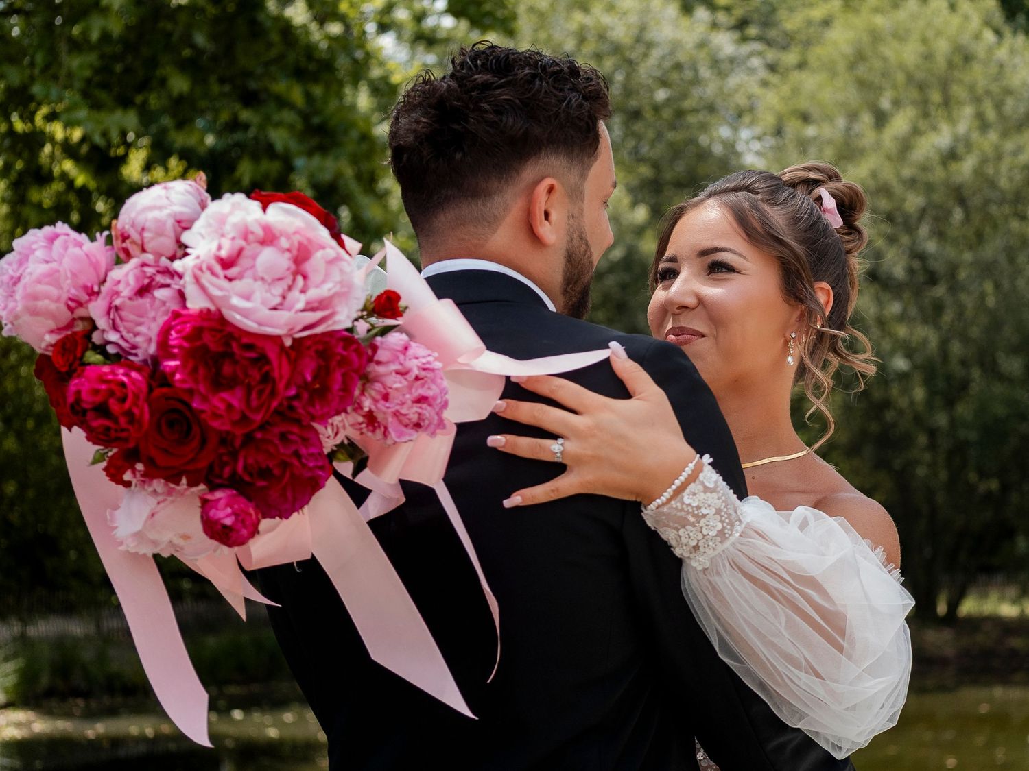 Wedding couple embracing outdoors surrounded by pink floral bouquets.