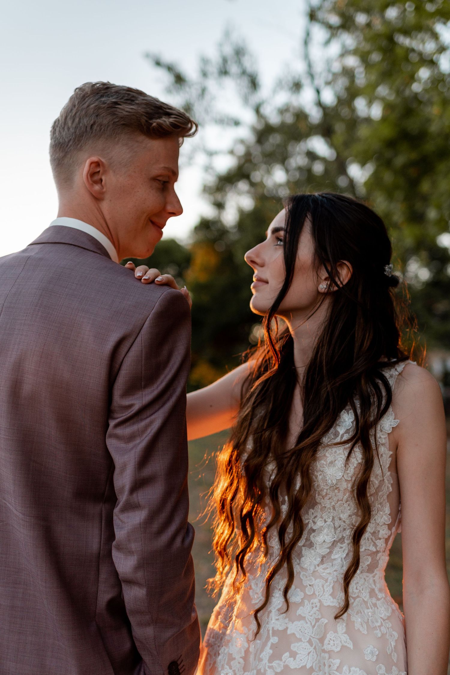 A romantic sunset wedding portrait shows a couple embracing in golden light with trees in the background.