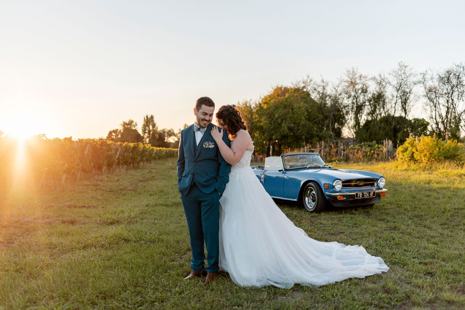 Wedding couple posing in a field at golden hour with vintage car in background.