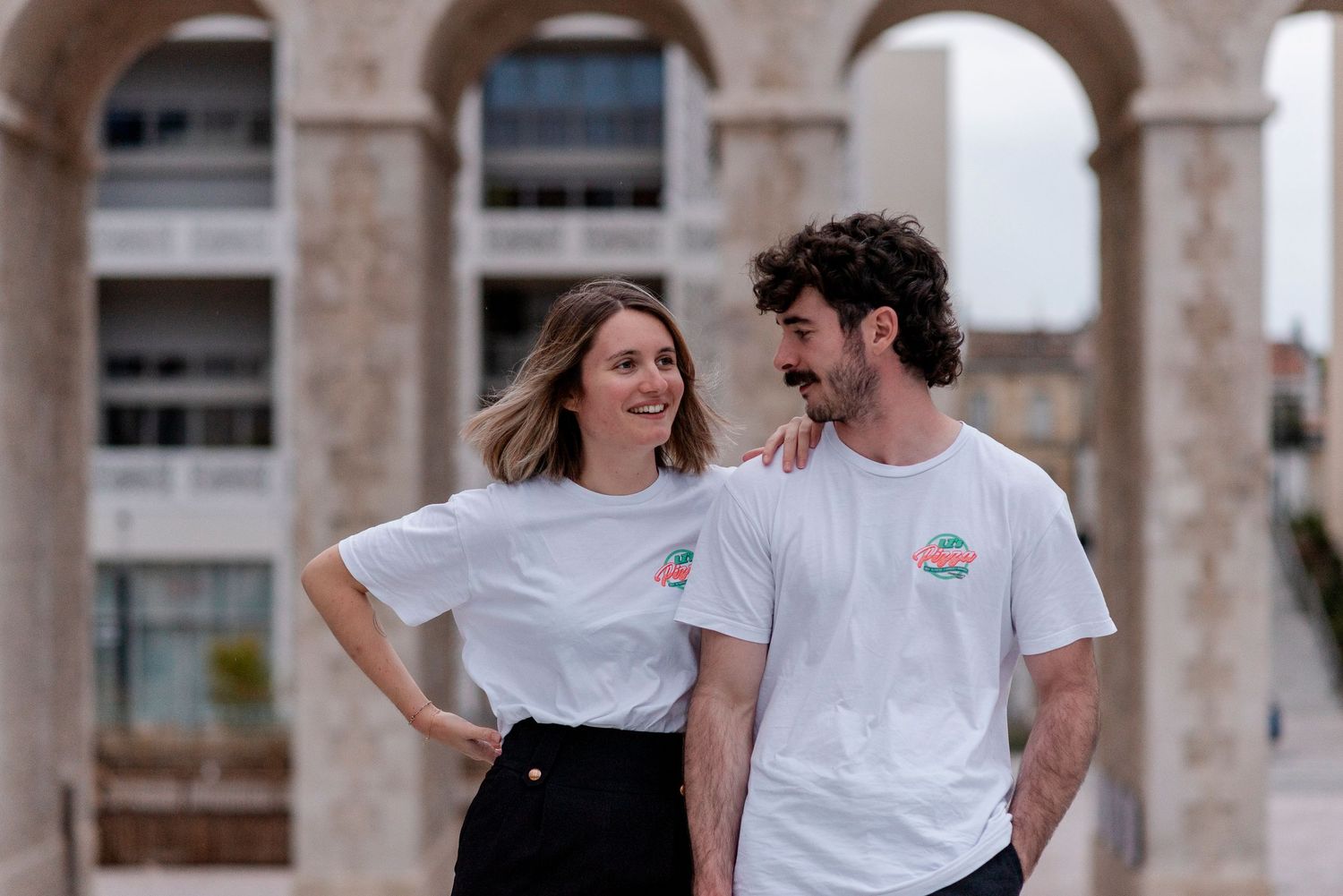 Couple laughing and walking together in front of classical stone archways.