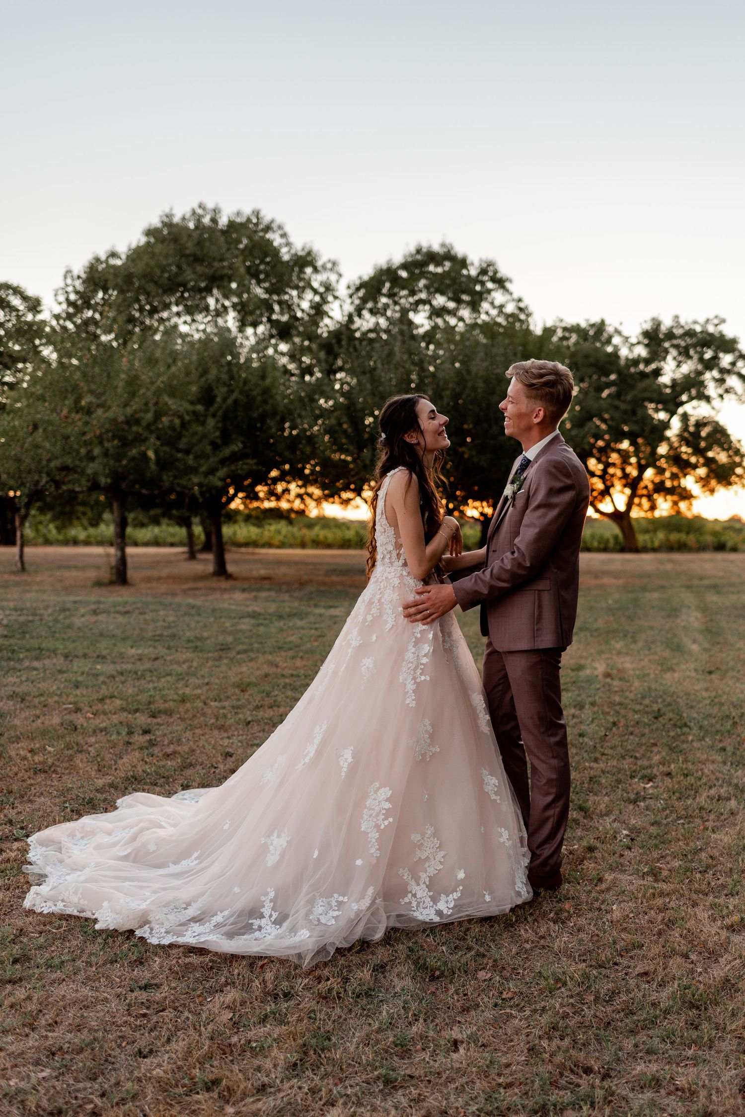 Romantic sunset wedding photo of newlyweds dancing together in a rustic orchard setting.