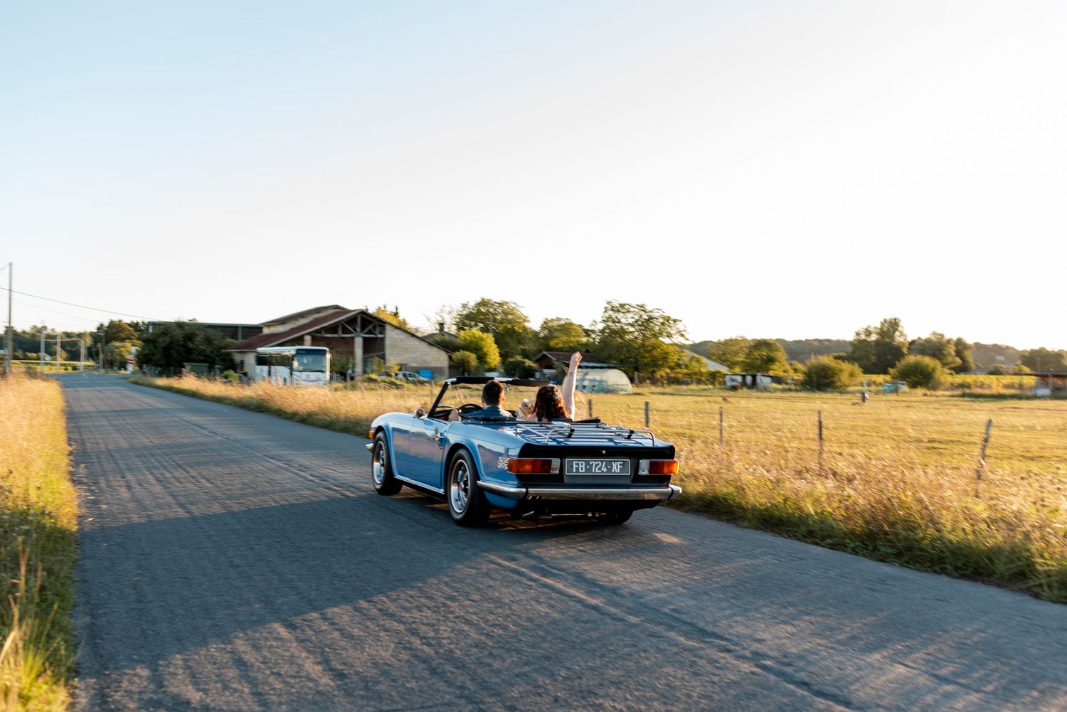 Classic blue convertible car parked on a rural road during sunset.