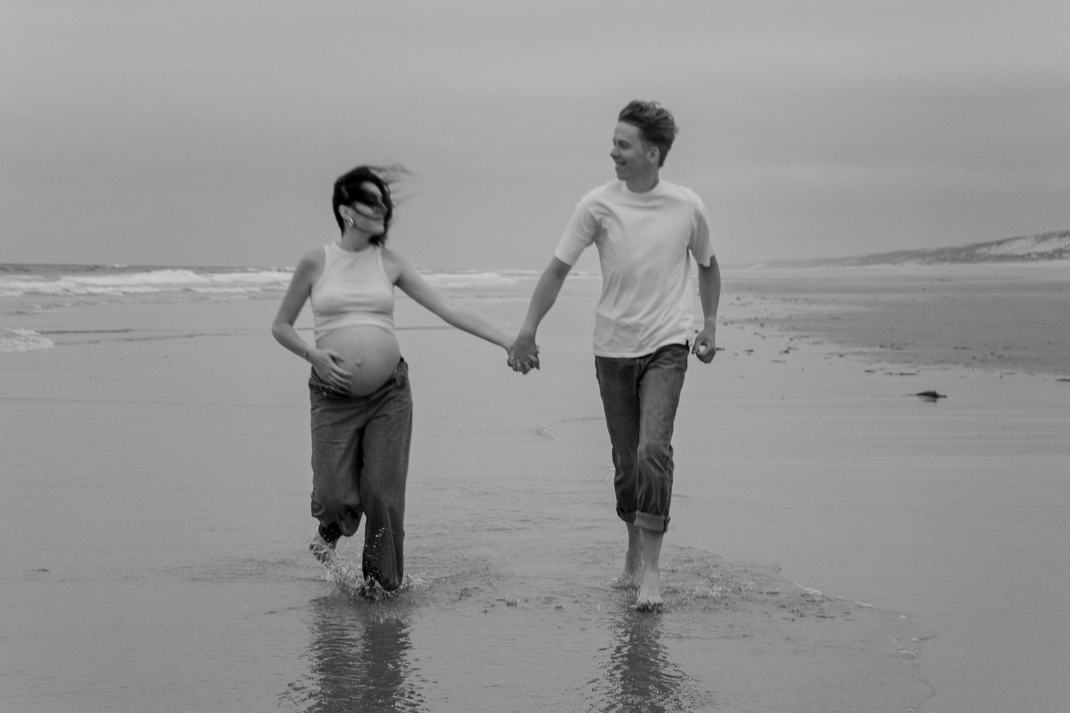 Playful couple splashing and running together in ocean waves at the beach.