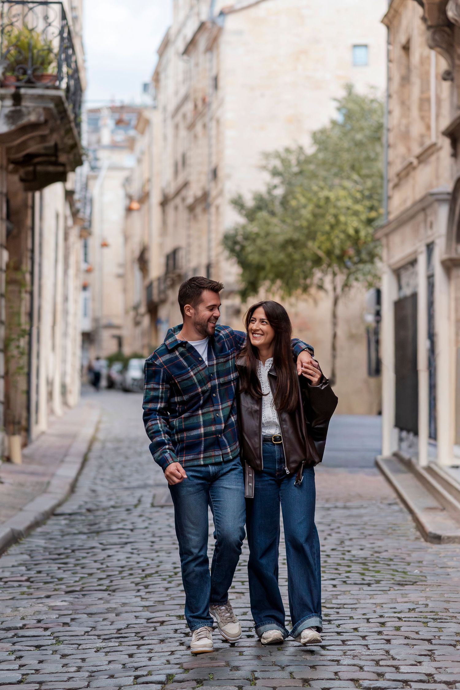 Couple walking and laughing together on cobblestone streets in a historic European town.