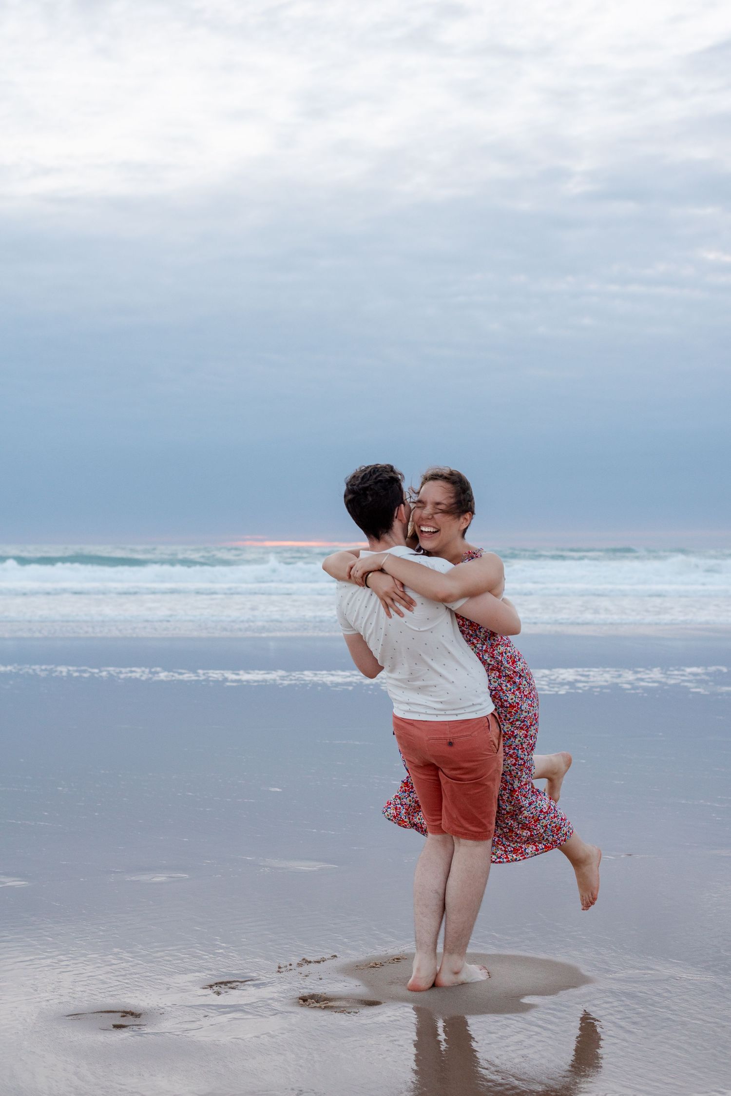 Playful couple enjoying time together on sandy beach with ocean waves in background.
