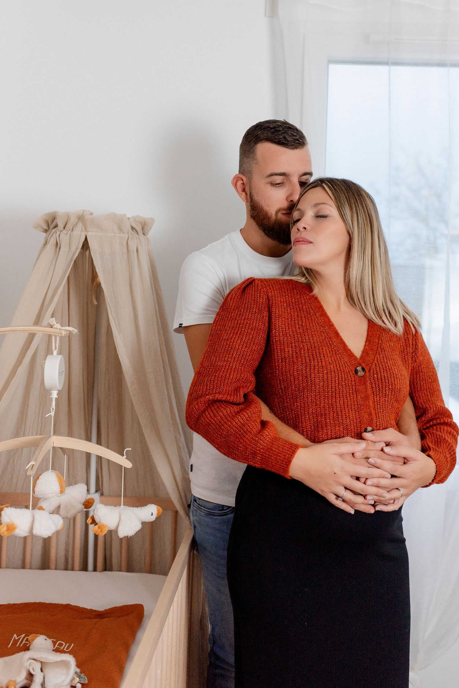 Couple sharing tender moment in cozy interior with rust-colored sweater and neutral decor.