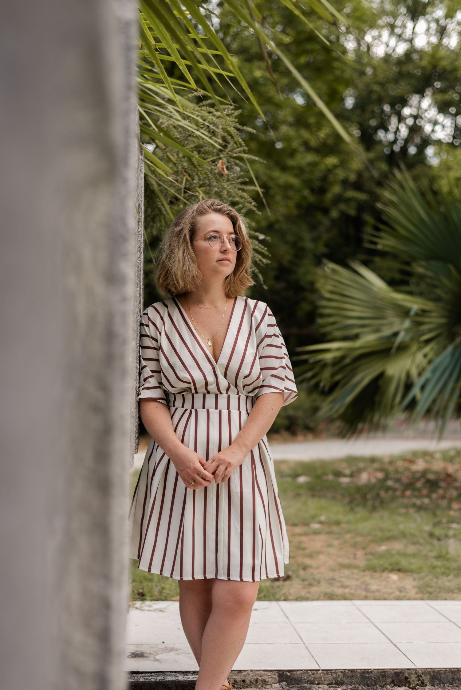 Portrait sequence of someone in a striped top posing outdoors near tropical plants.