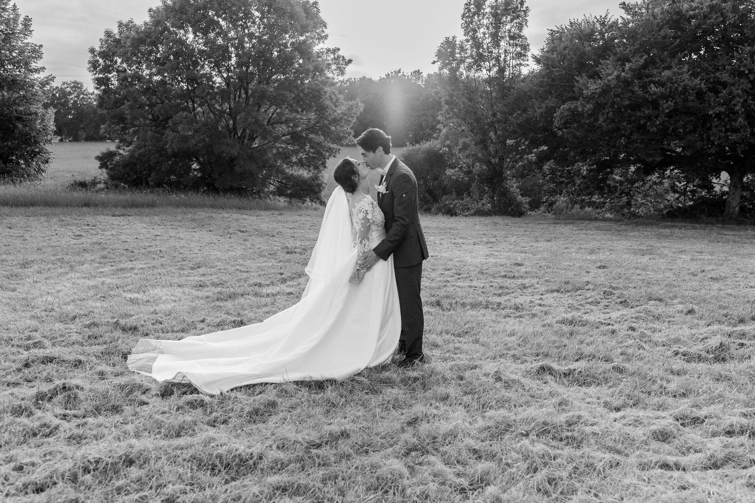 Black and white wedding photos capture romantic moments in a sunlit meadow.