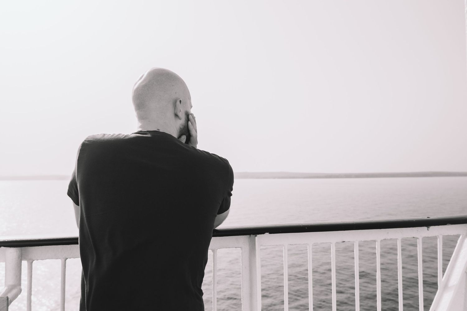 Black and white panoramic view of people sitting on a railing overlooking water.