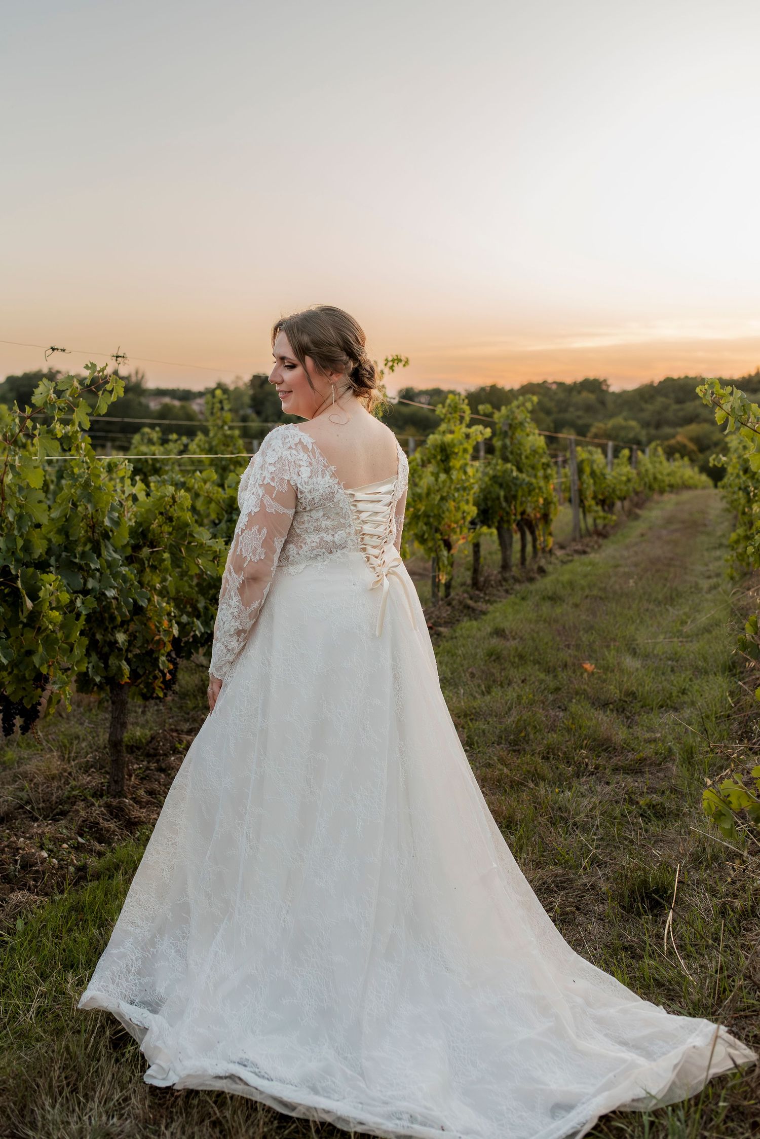 Beautiful lace wedding dress with long train photographed in a vineyard at sunset.
