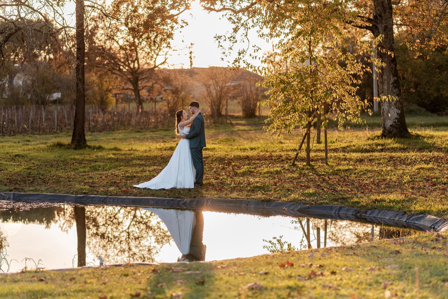 Wedding couple poses in a scenic autumn park with pond reflections at sunset.