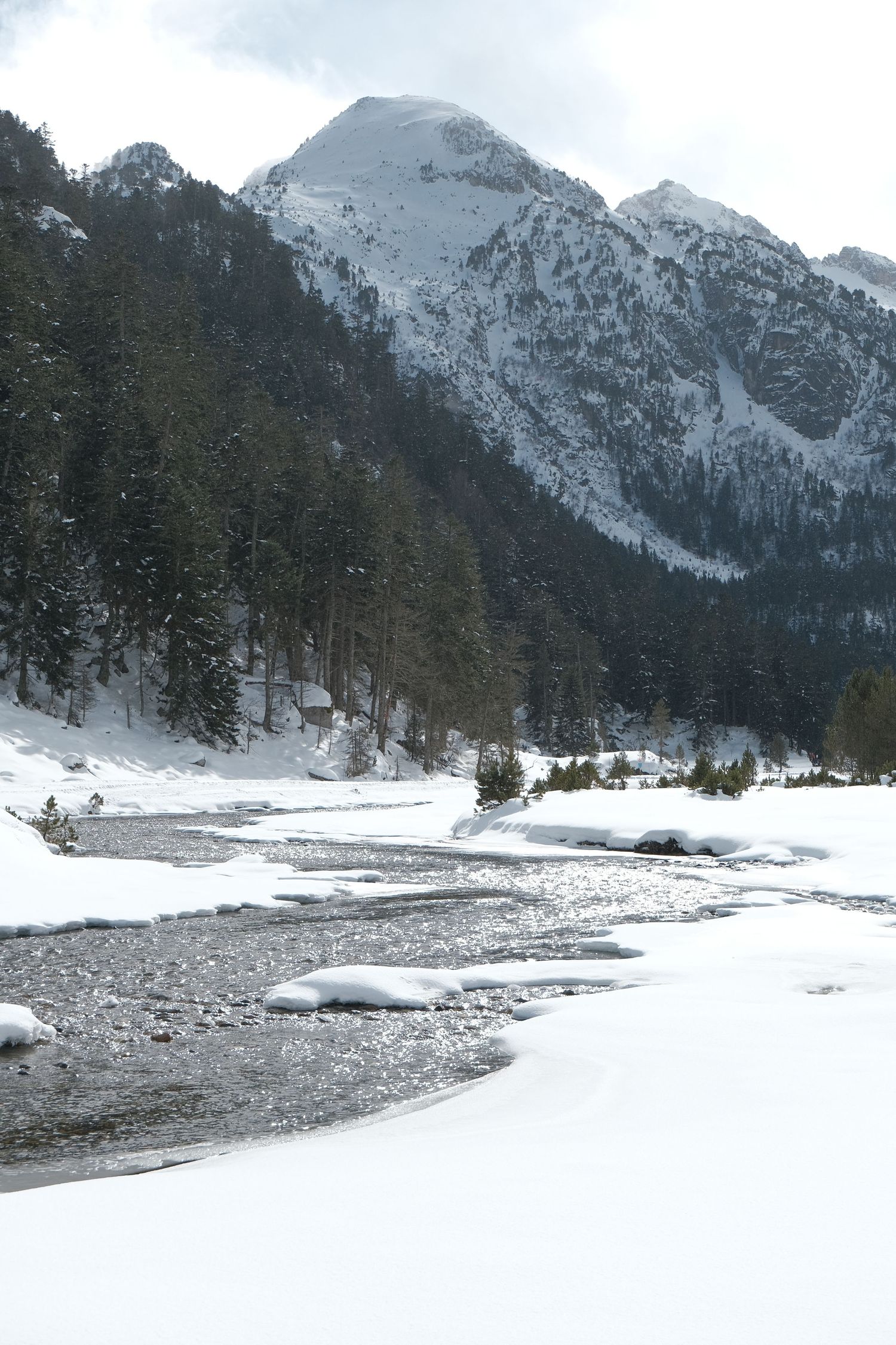 Snow-covered mountain landscape with winding river and evergreen trees.
