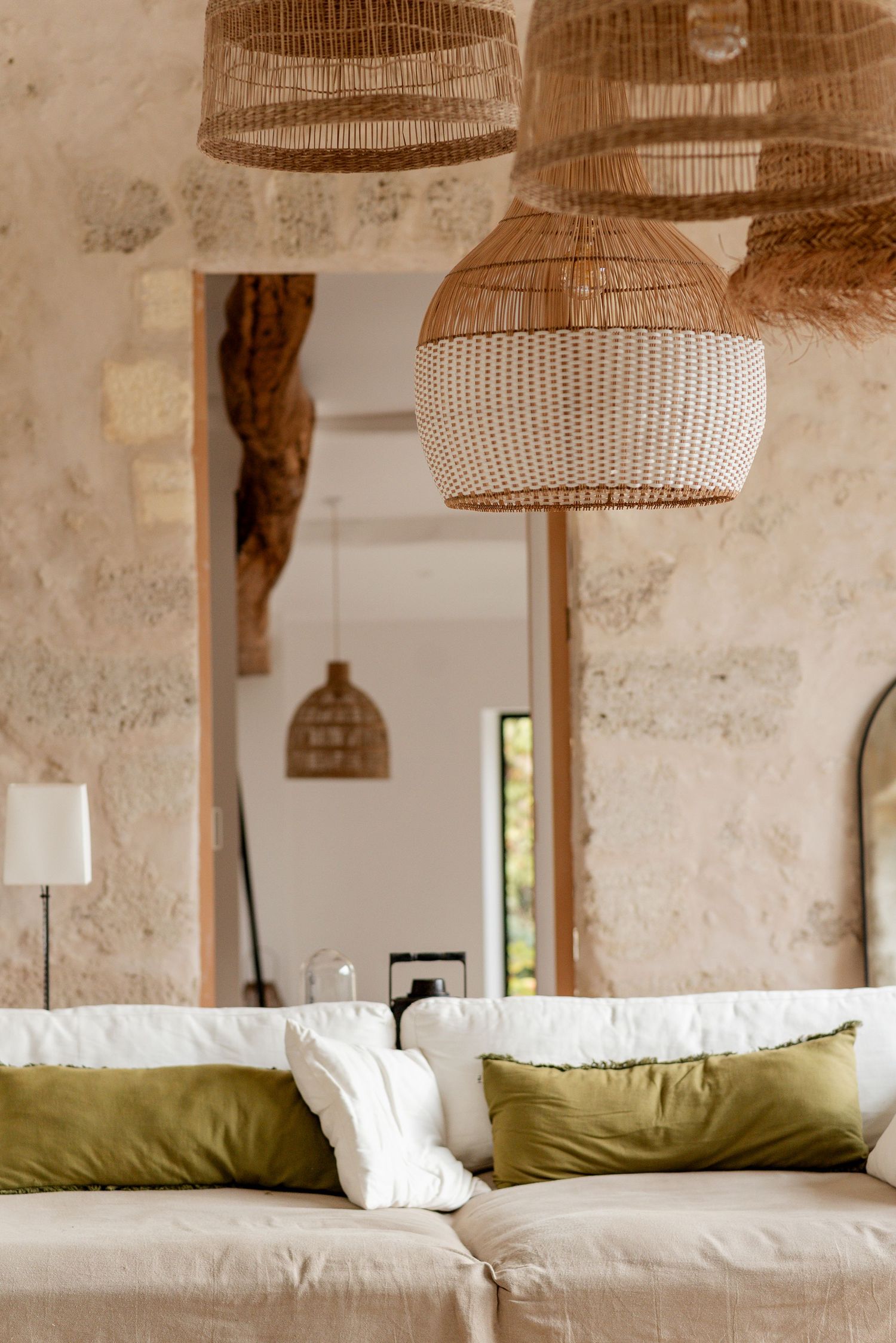 Modern rustic room with woven pendant lamps and white cushioned seating against stone walls.