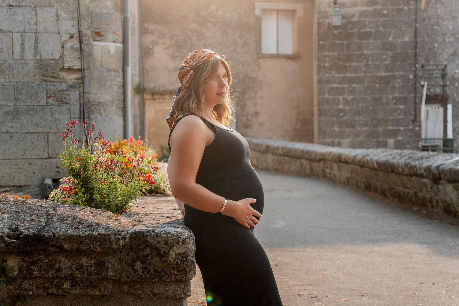 Maternity photoshoot in warm sunset light against stone wall backdrop.