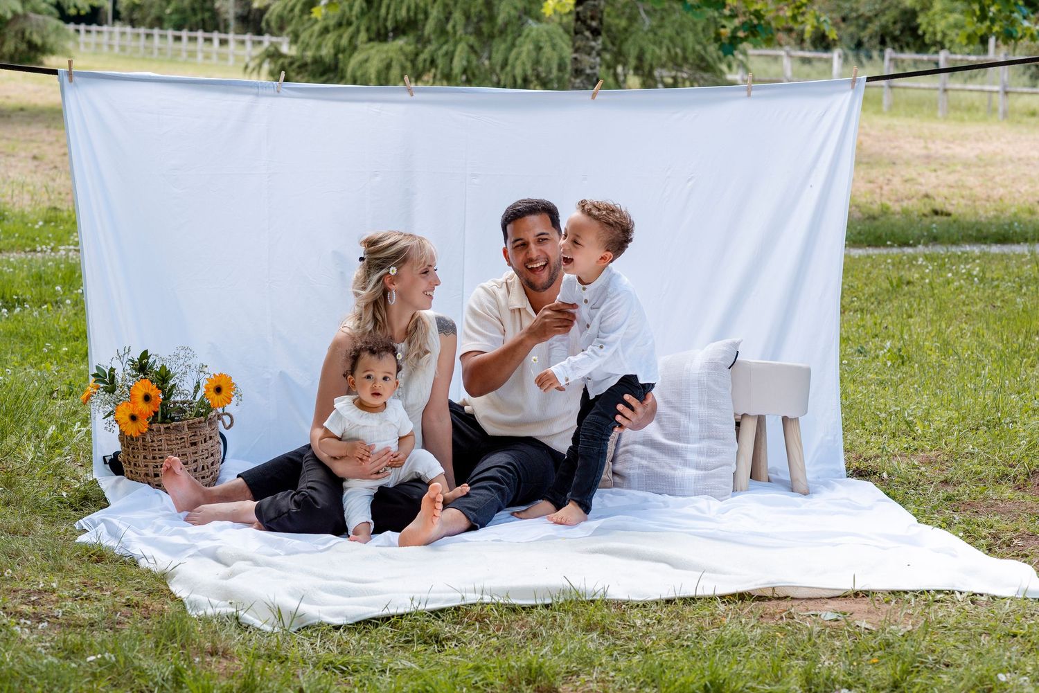 Family photo session on white blanket with sunflowers and outdoor backdrop.