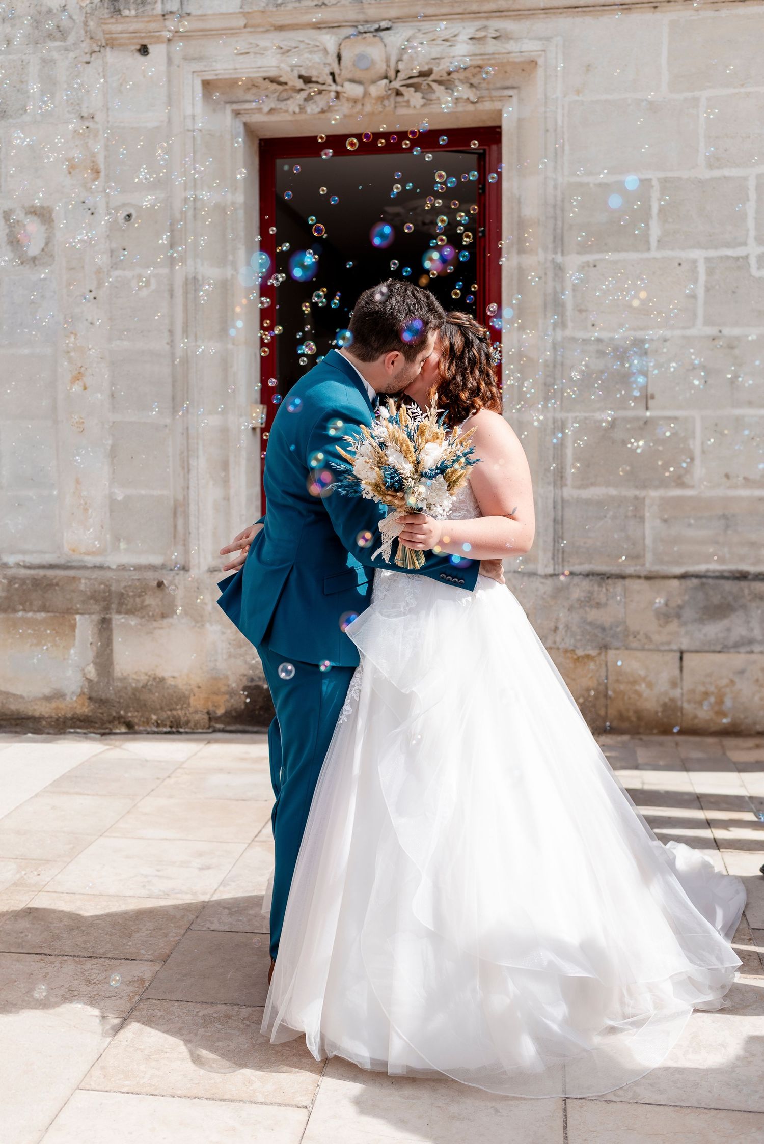 Wedding couple shares romantic moment with bubbles floating around stone archway.