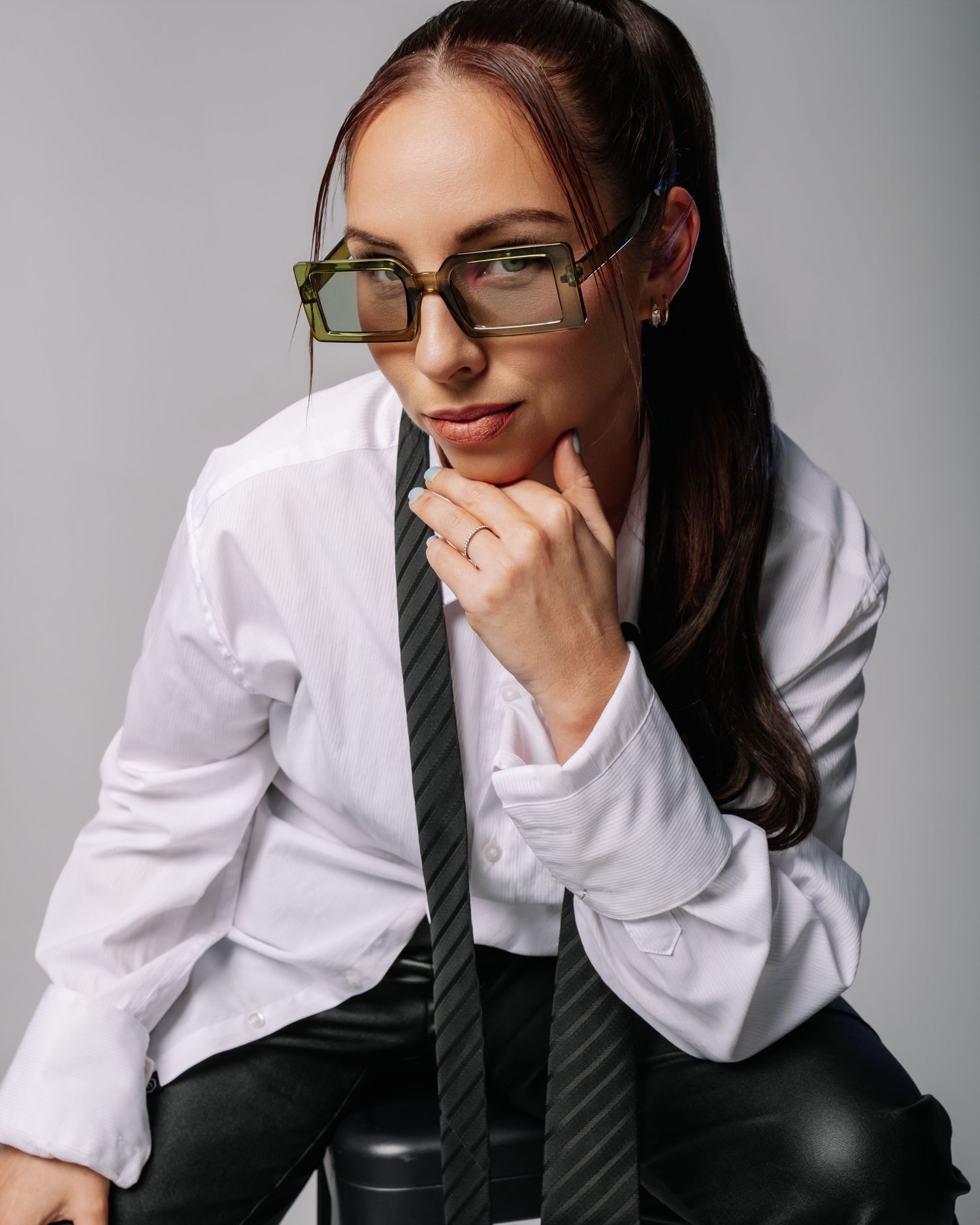 A professional wearing a white button-down shirt and dark tie leans thoughtfully against a grey background.