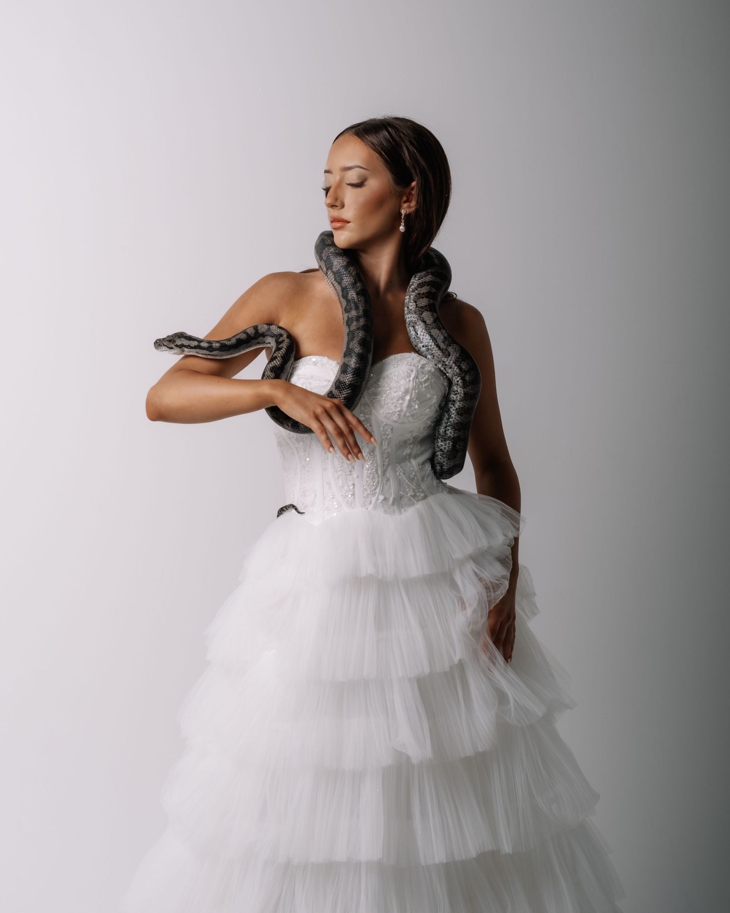 A bride in a voluminous tiered tulle ball gown poses gracefully in a studio setting.
