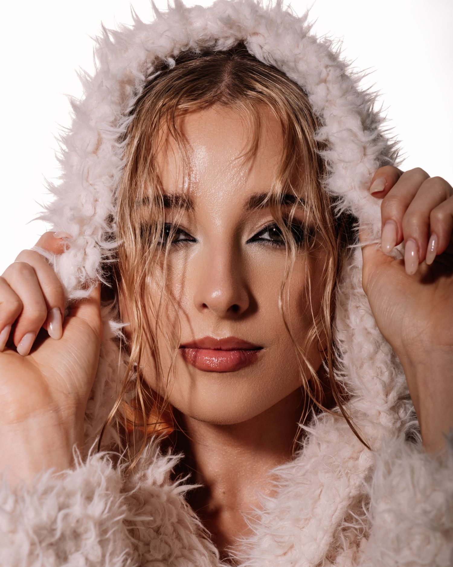Close-up portrait of woman with wet hair wearing fluffy hooded coat against white background.