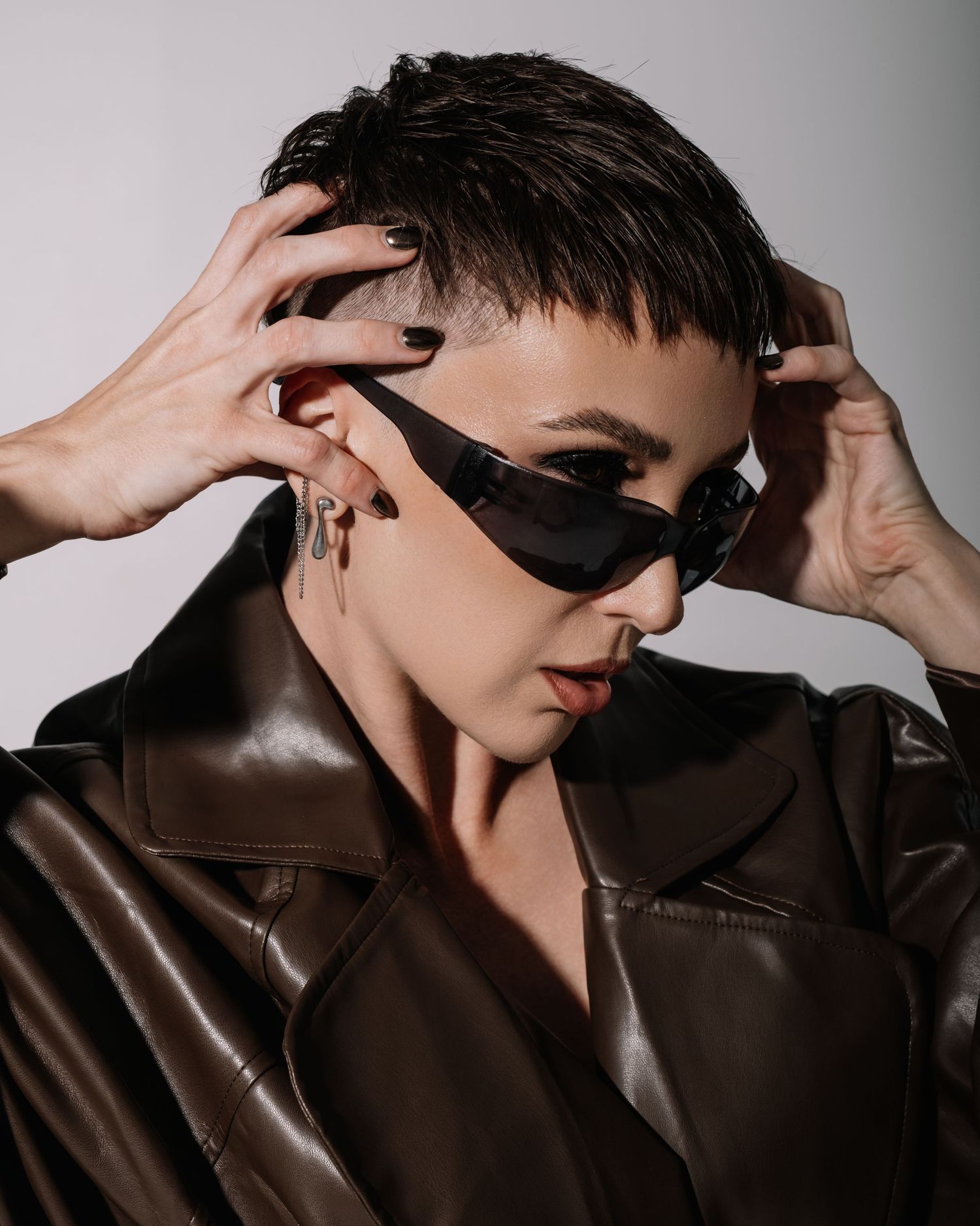 Person in dark sunglasses and brown leather jacket shown in multiple poses against a grey background.