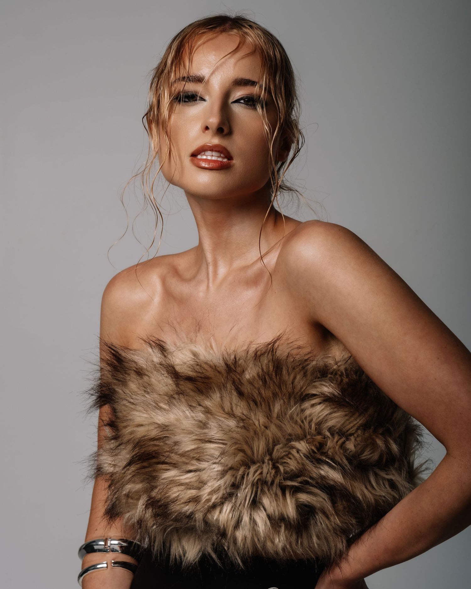 A fashion model poses elegantly in a brown fur wrap against a neutral studio backdrop.