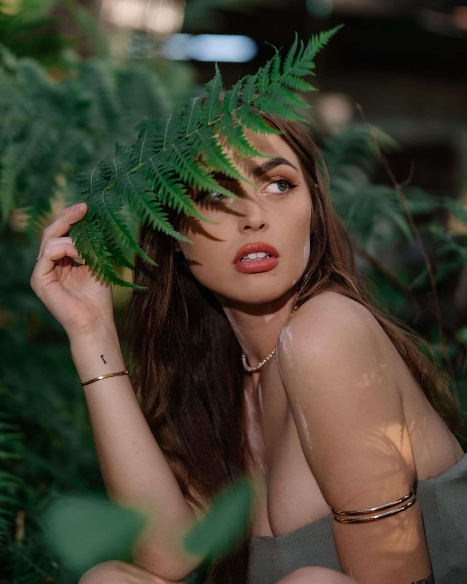 A sensual portrait among ferns and greenery with dramatic lighting and natural shadows.