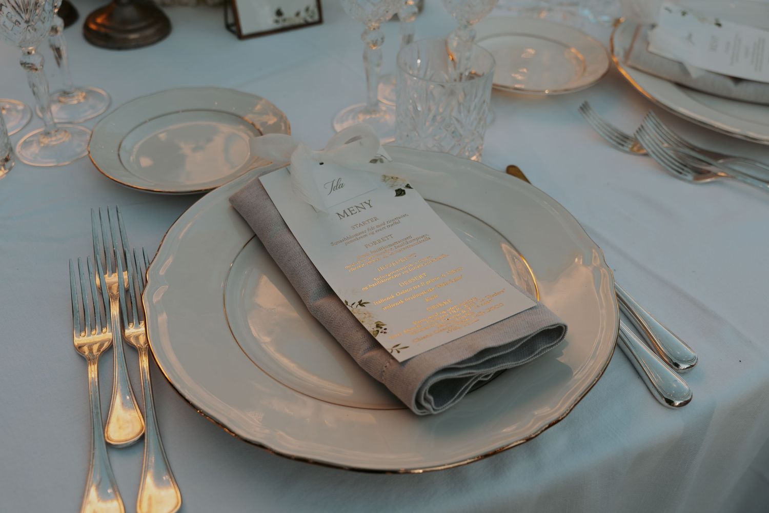 Close-up of formal place settings with white plates, silver cutlery, and folded napkins on a light tablecloth.