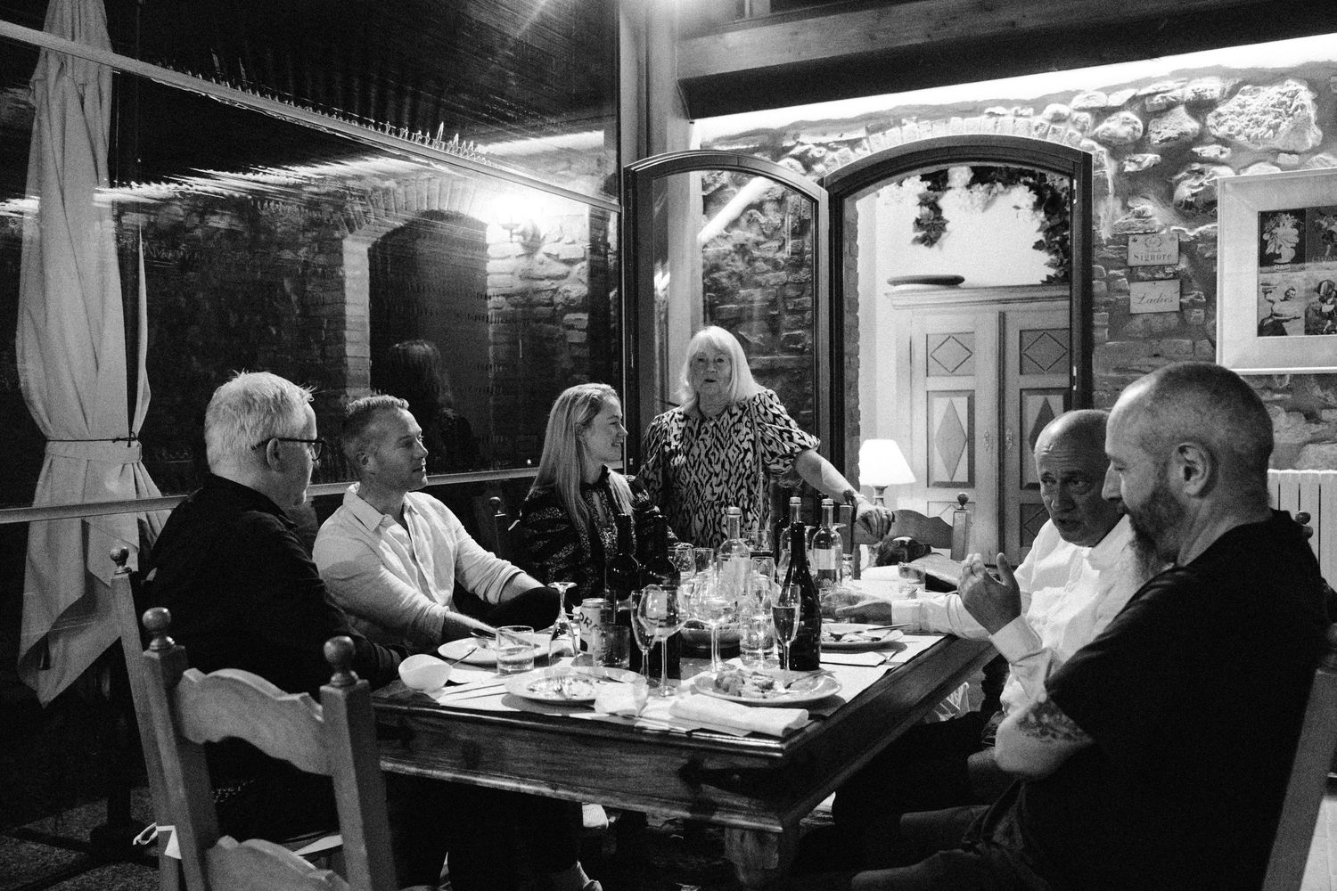 An evening dinner gathering with wine and conversation under outdoor lighting.