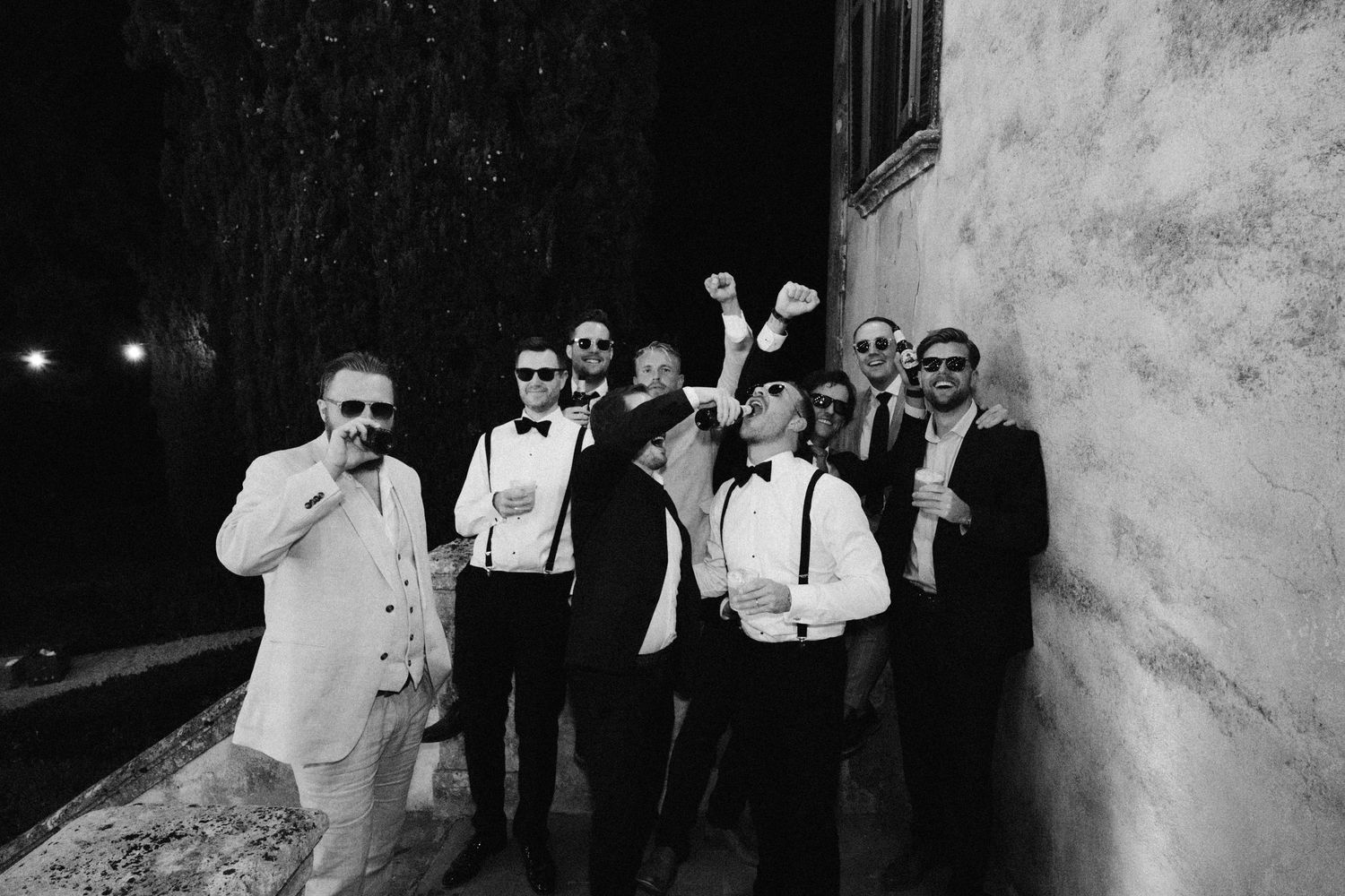 Wedding party posing against textured wall in dramatic black and white photography.