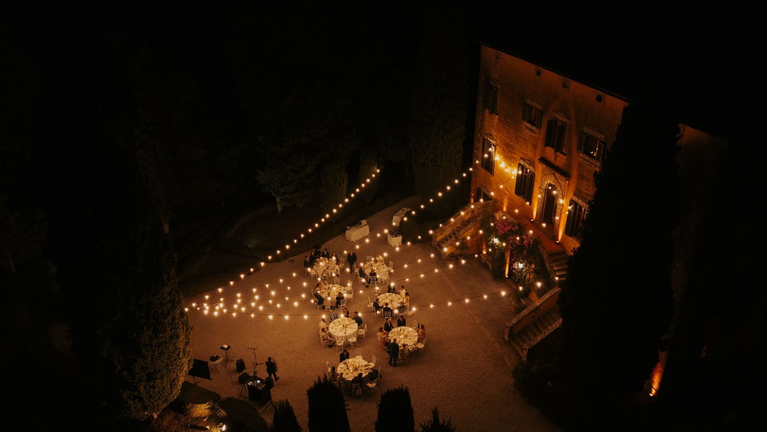 String lights illuminate an outdoor wedding venue against the dark night sky.