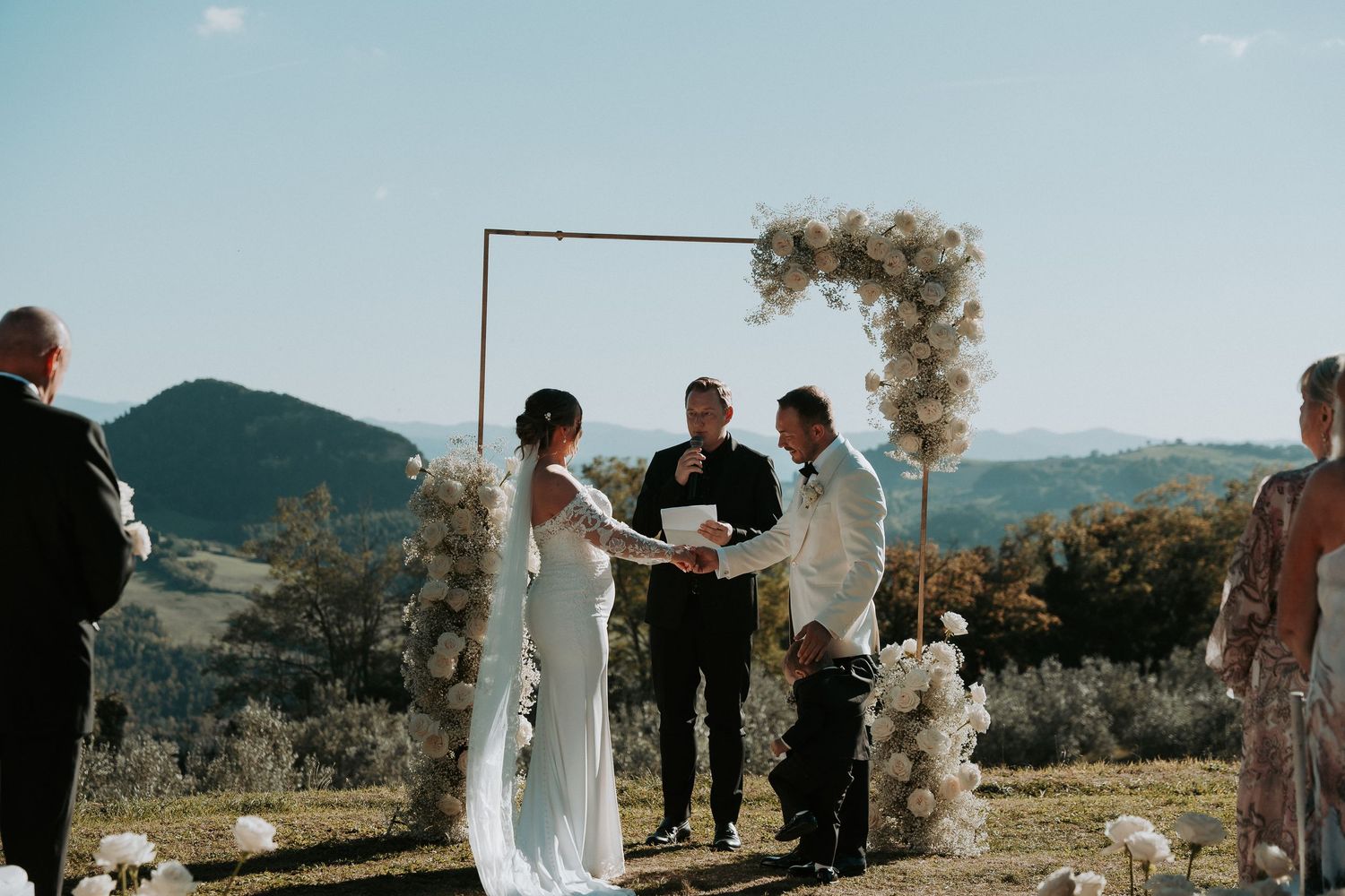 Outdoor wedding ceremony with mountain views and floral arch against blue sky.
