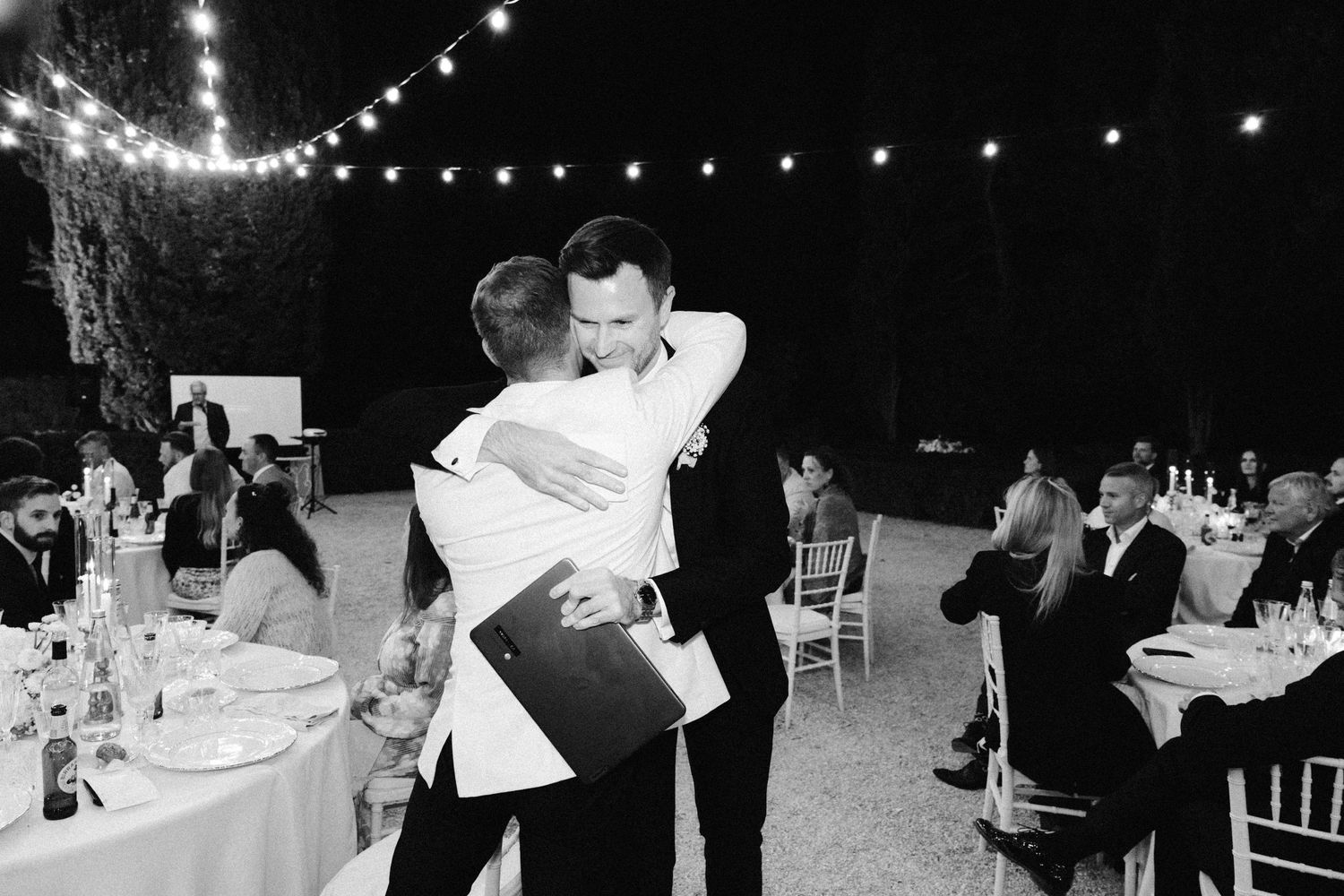 Black and white photo of servers carrying plates at an elegant outdoor wedding reception.