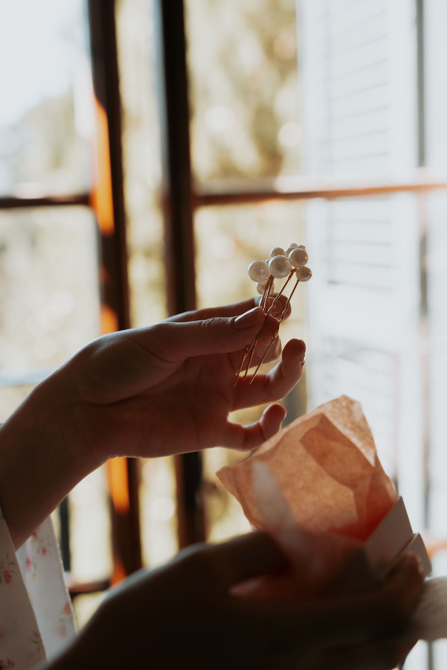 Delicate hands hold up a sheer fabric against sunlit windows creating a soft, ethereal effect.