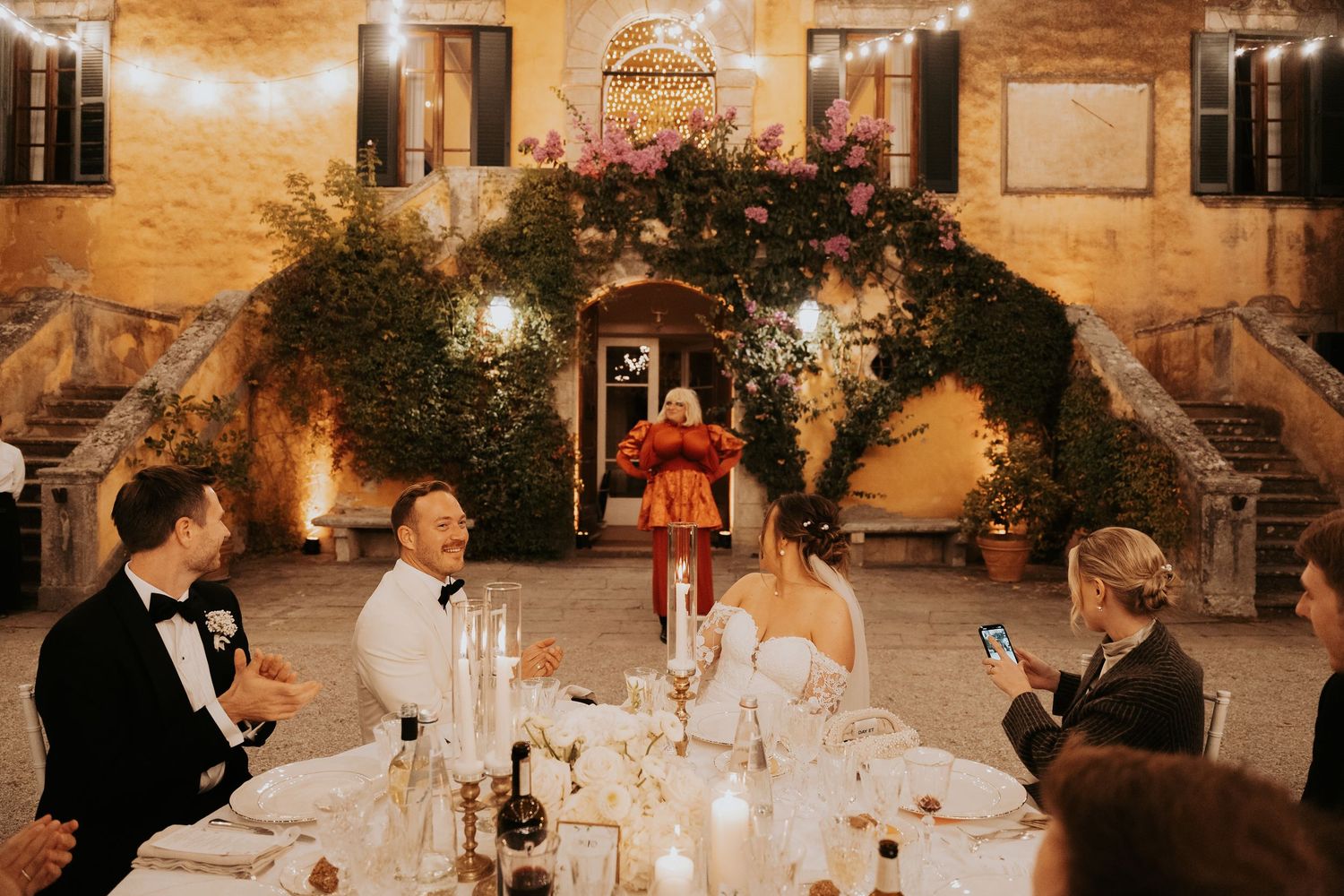 Wedding reception dinner setup with elegant table settings and warm lighting against stone walls.