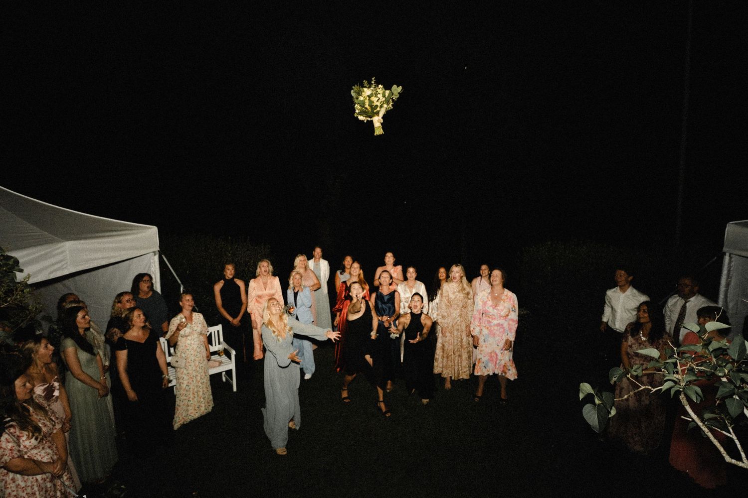 Wedding reception guests celebrating at night under outdoor lighting.