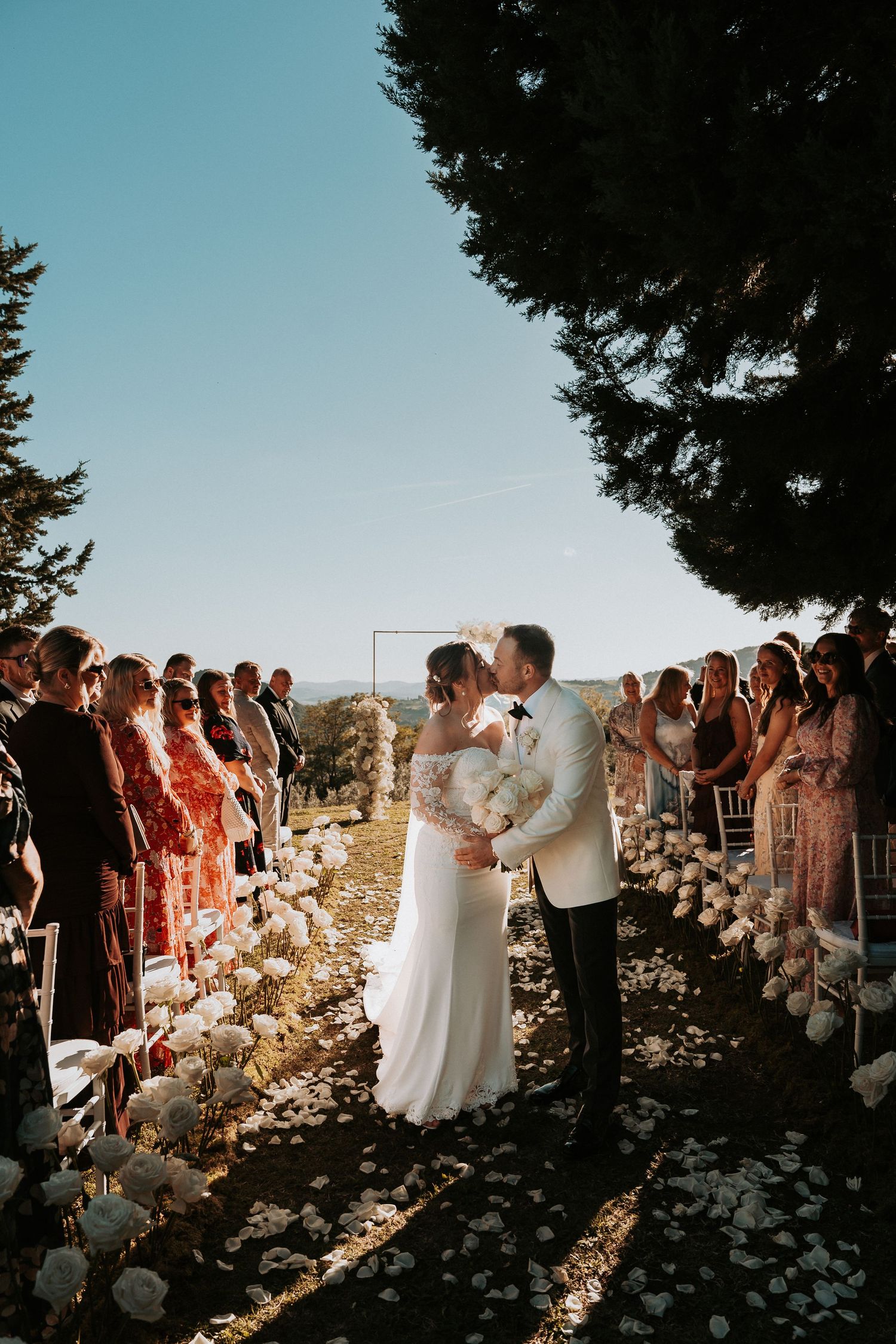 Sunset wedding ceremony with flower petals lining the aisle and guests watching from both sides.