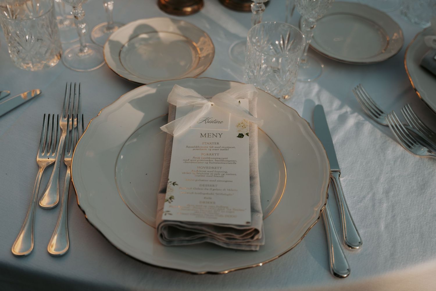 Close-up of formal place settings with menu cards and silverware at wedding reception.