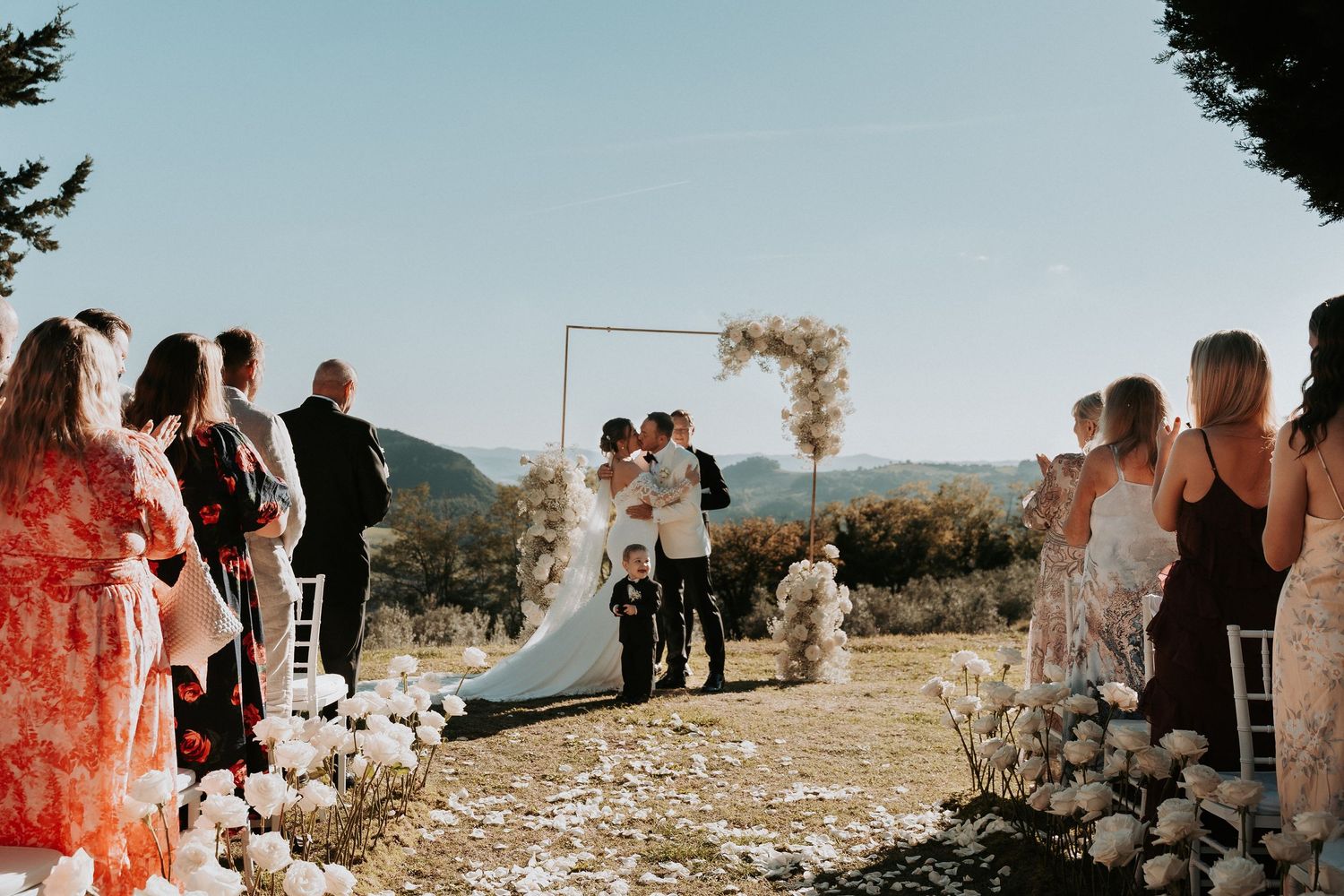 Wedding ceremony with guests lined up along a petal-strewn aisle against mountain backdrop.