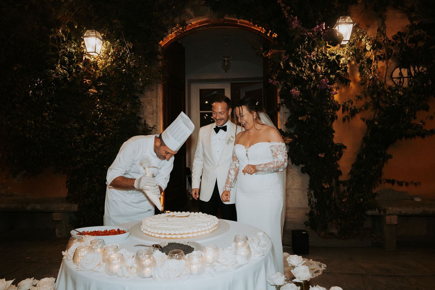 Wedding cake cutting ceremony with chef and couple under an illuminated archway.