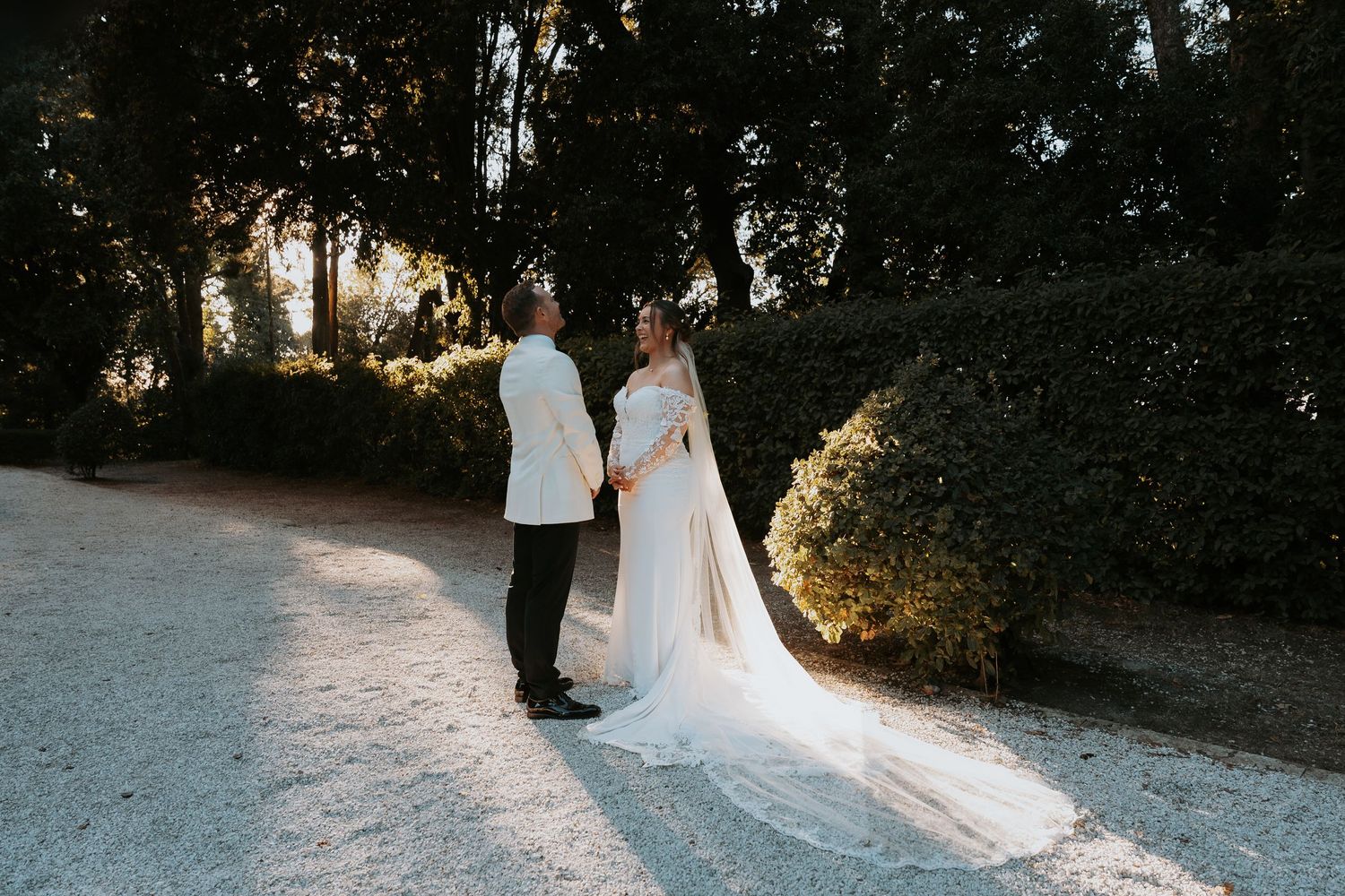 Wedding couple walks along a sunlit garden path at dusk.