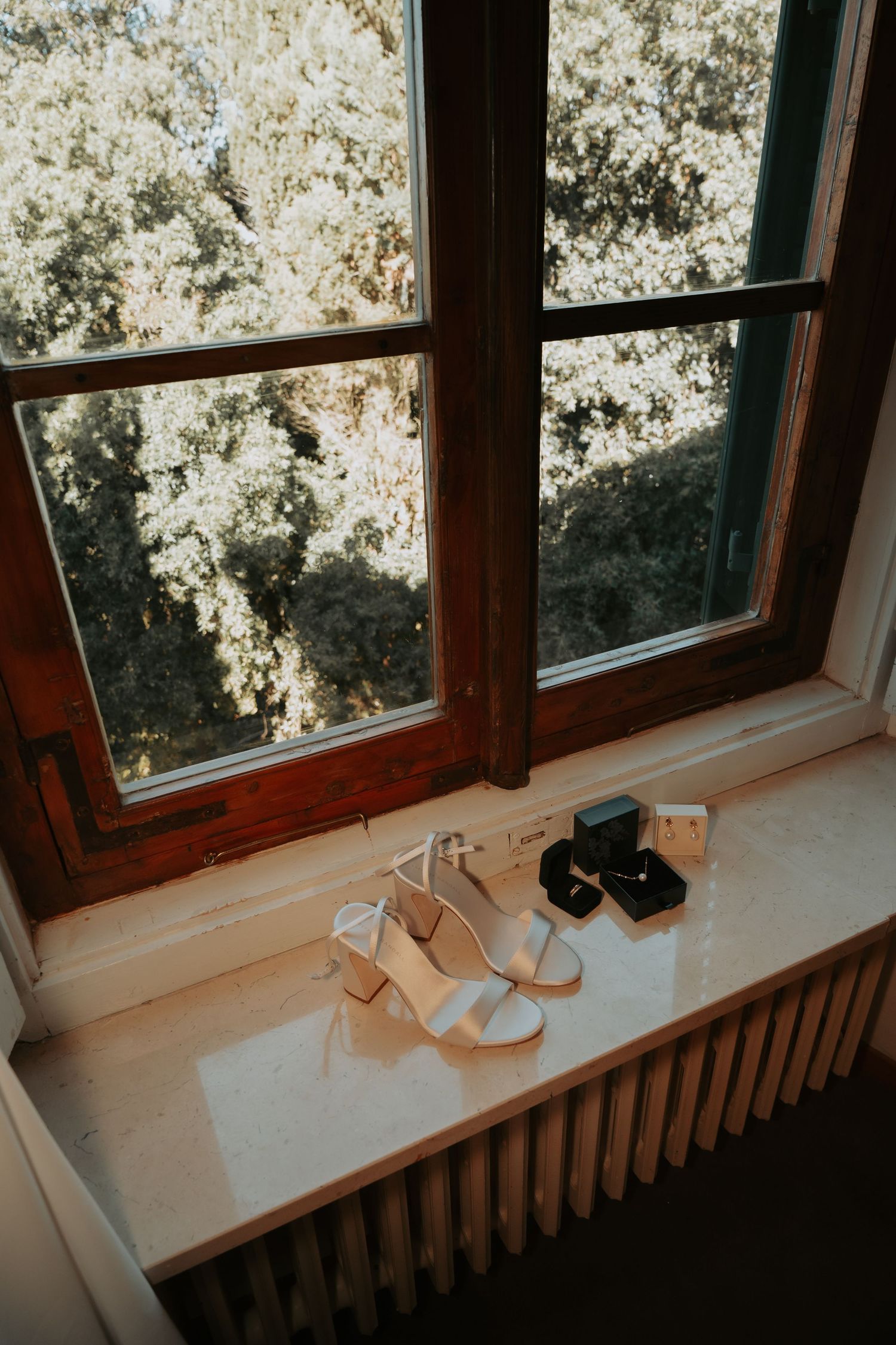 Wooden-framed windows with white curtains and shoes placed on a windowsill with radiator below.