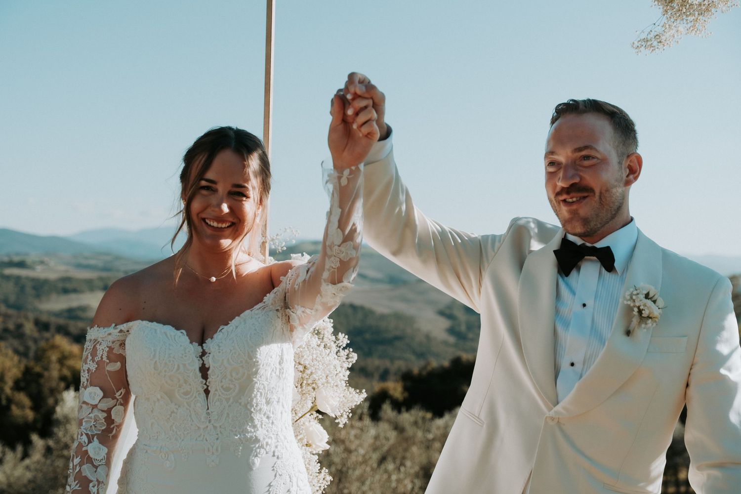 Newlyweds celebrate with raised hands against scenic mountain backdrop.