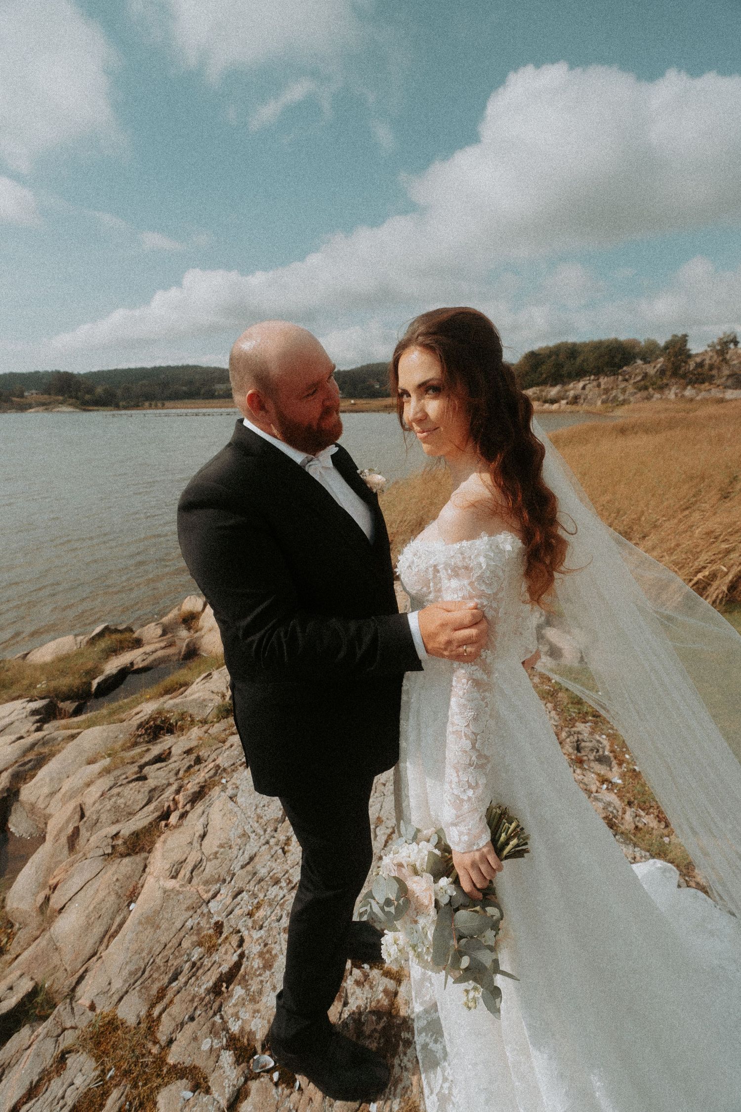 A romantic wedding photoshoot on rocky coastal cliffs with dramatic cloudy skies in the background.