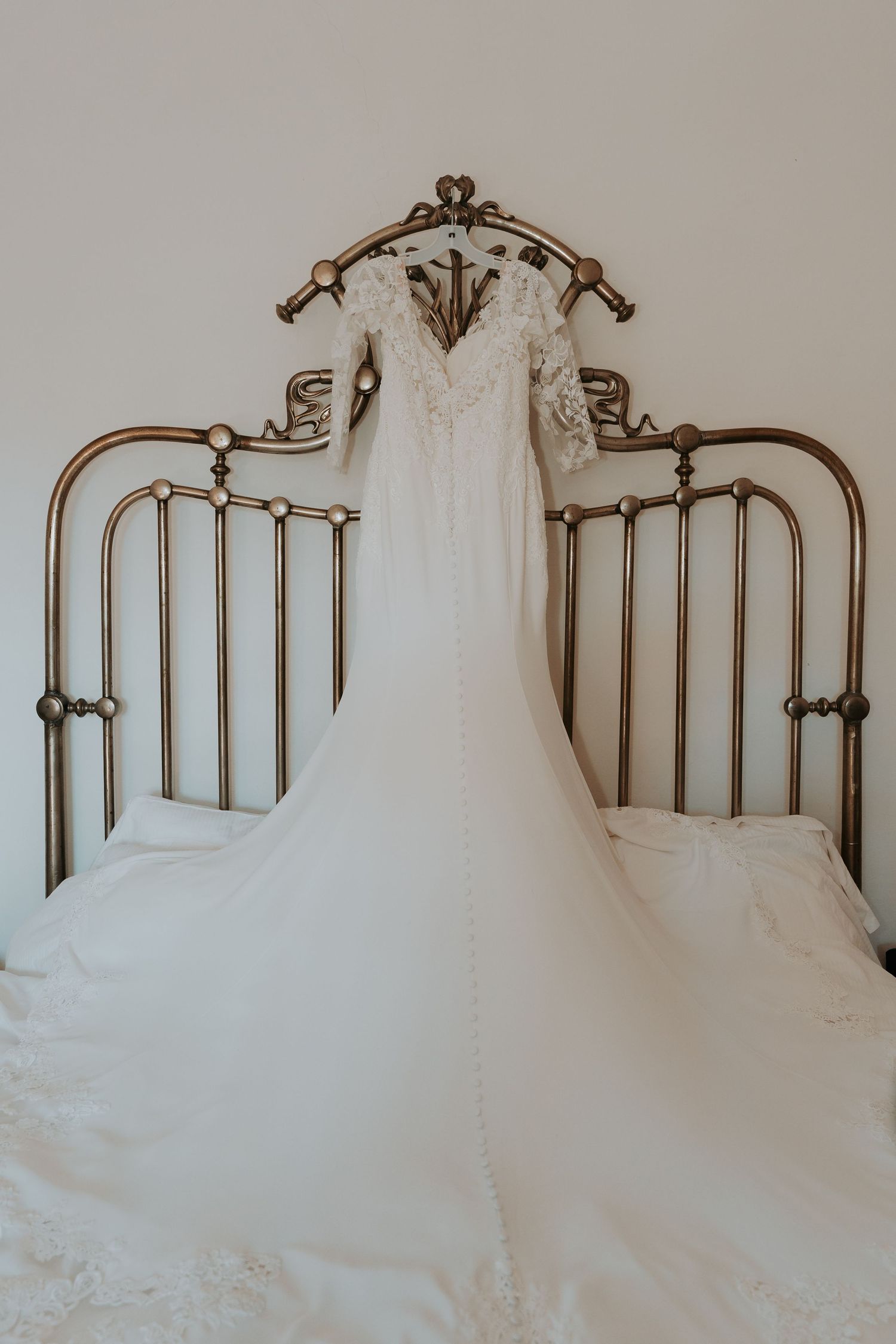 Elegant white wedding dress laid out on an antique brass bed frame.