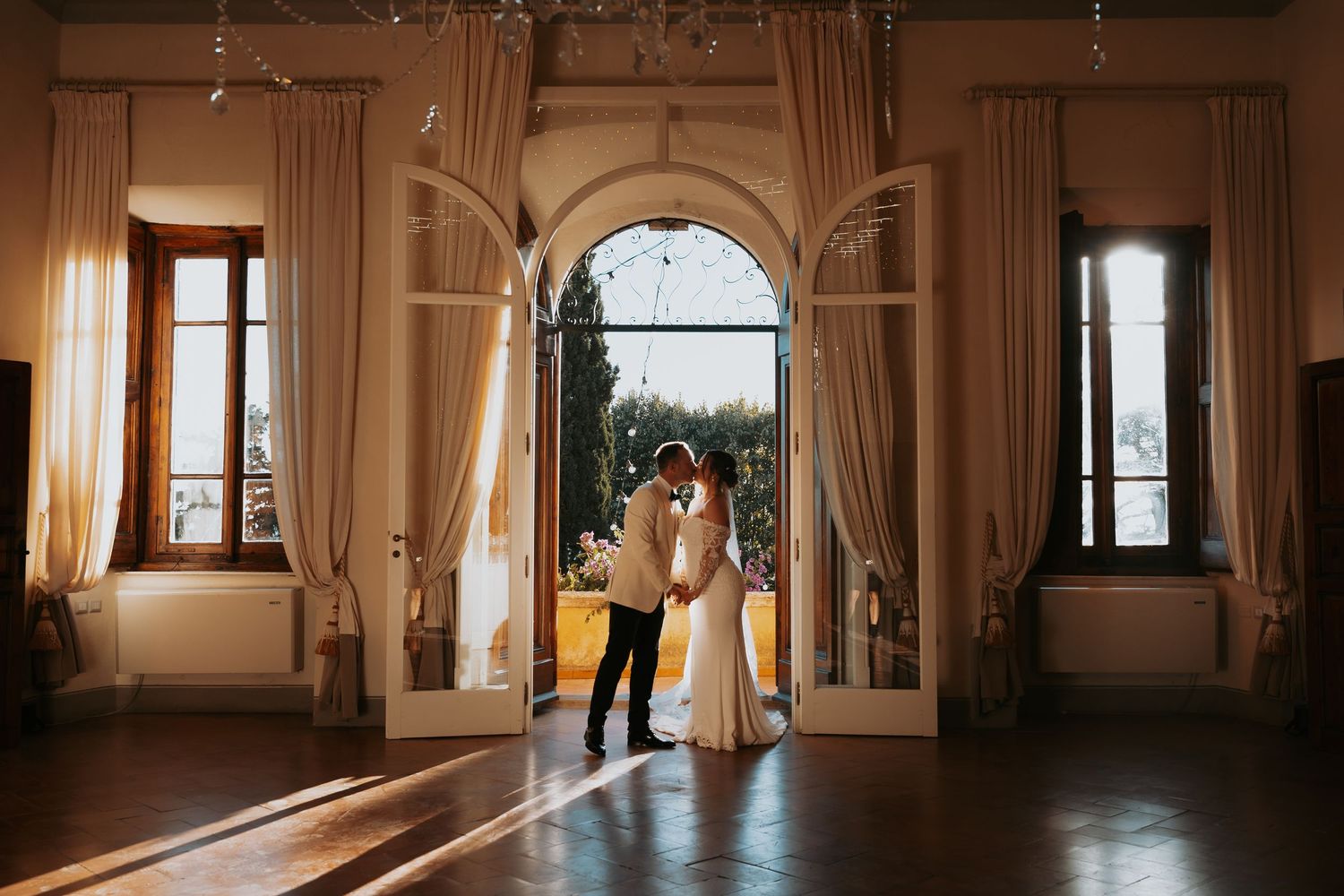 Wedding couple embraces in an elegant room with arched doorways and natural light.
