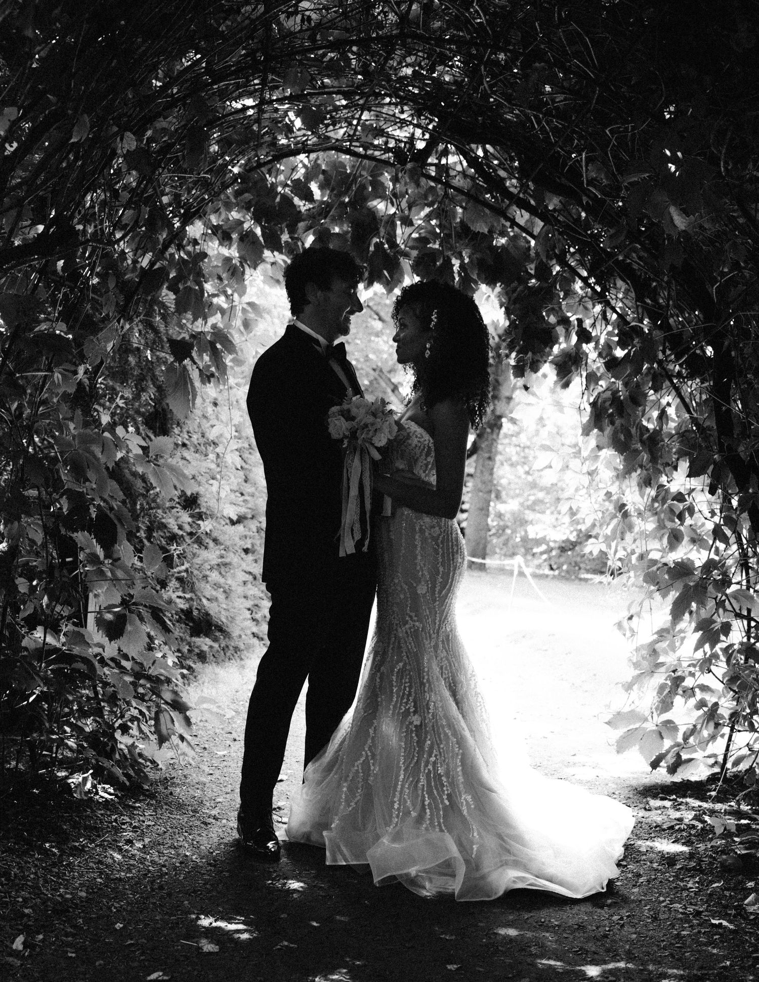 Black and white romantic wedding photos showing a couple in a garden setting under tree canopies and stone walls.