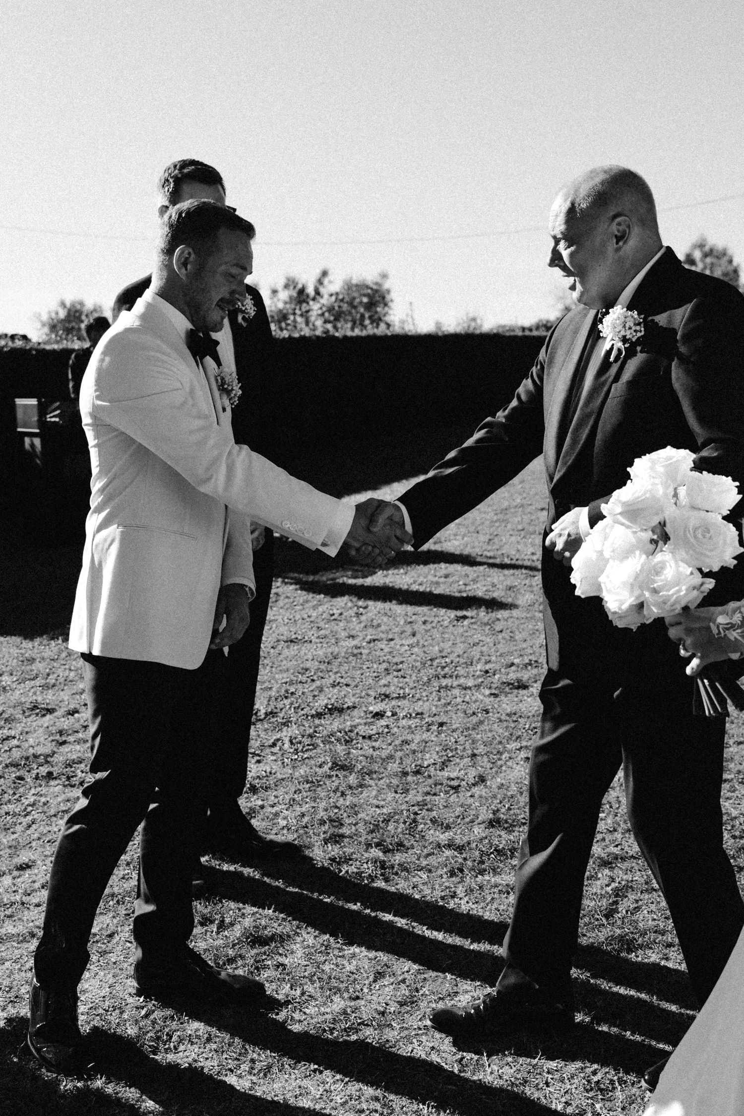 Black and white photo of two people in formal attire shaking hands at an outdoor event.