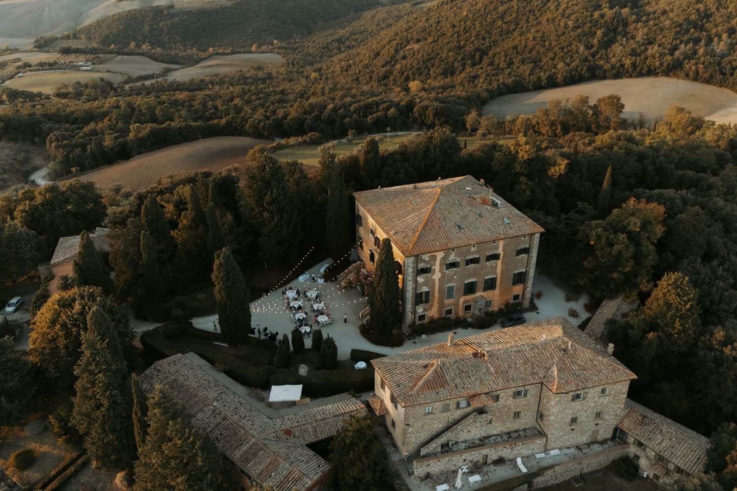 Aerial view of a Tuscan-style villa wedding venue nestled in rolling countryside hills.