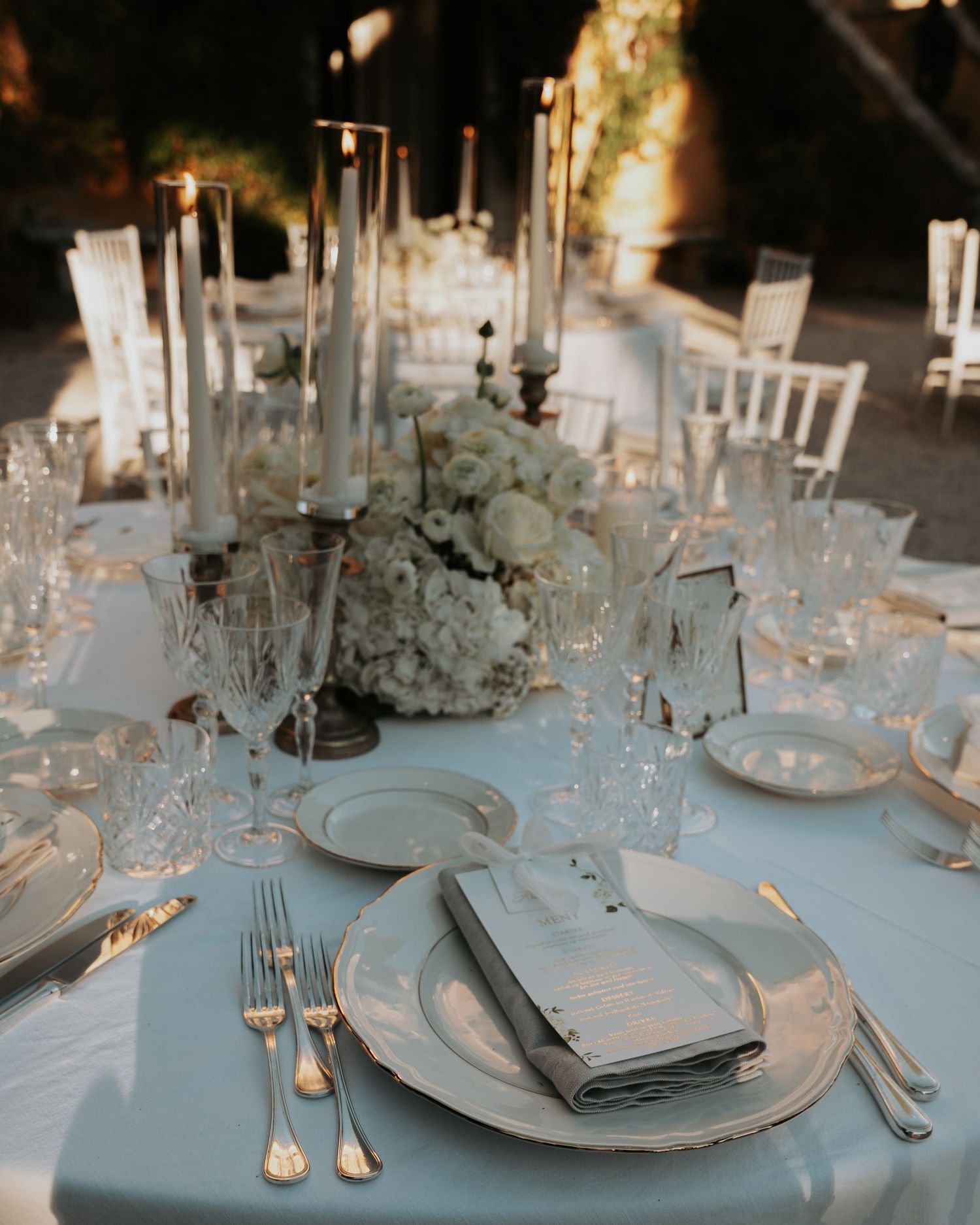 Elegant wedding reception table settings with white linens, fine china, and crystal glassware create a sophisticated atmosphere.