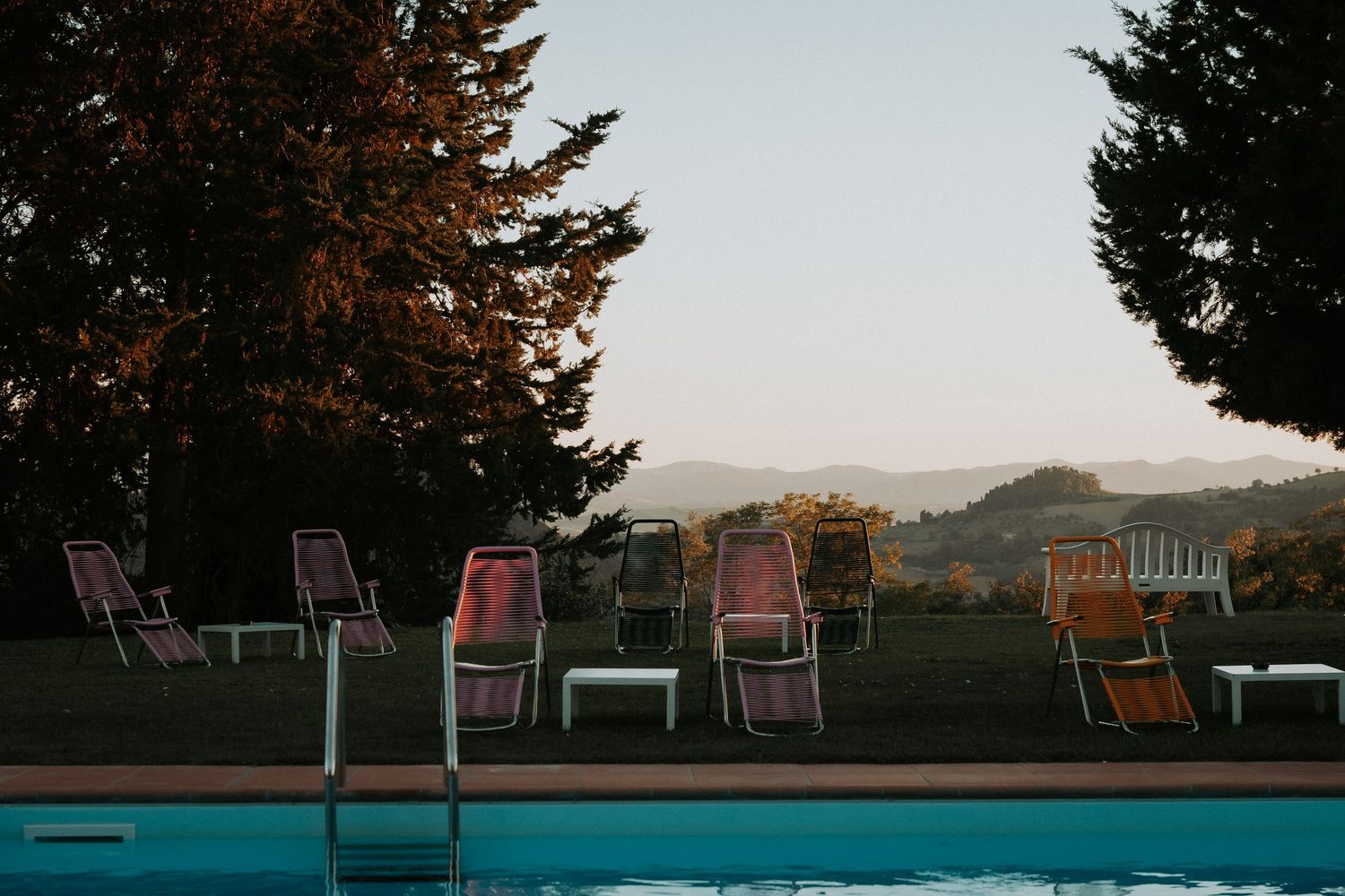 Empty lounge chairs arranged around a swimming pool at sunset.